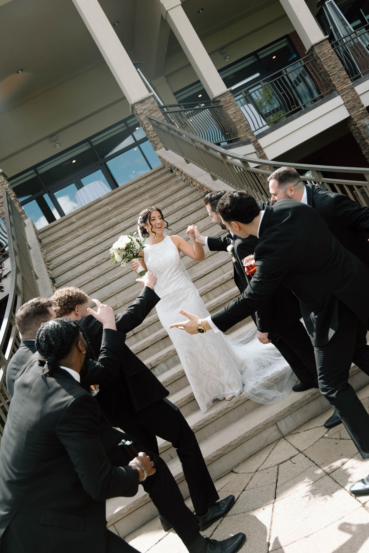 A couple in wedding attire playfully poses on grand stone steps during a photo session.