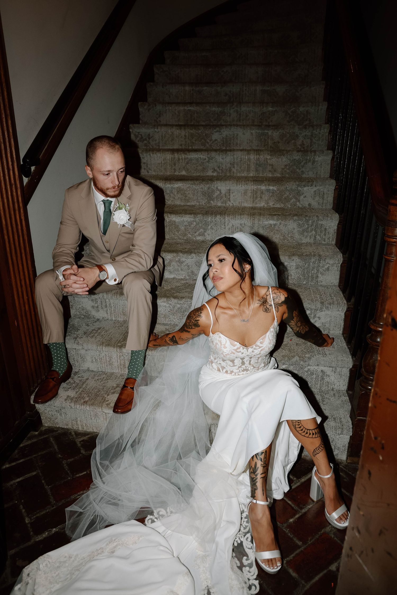 A bride in a white gown sits gracefully on elegant stone steps during a wedding.