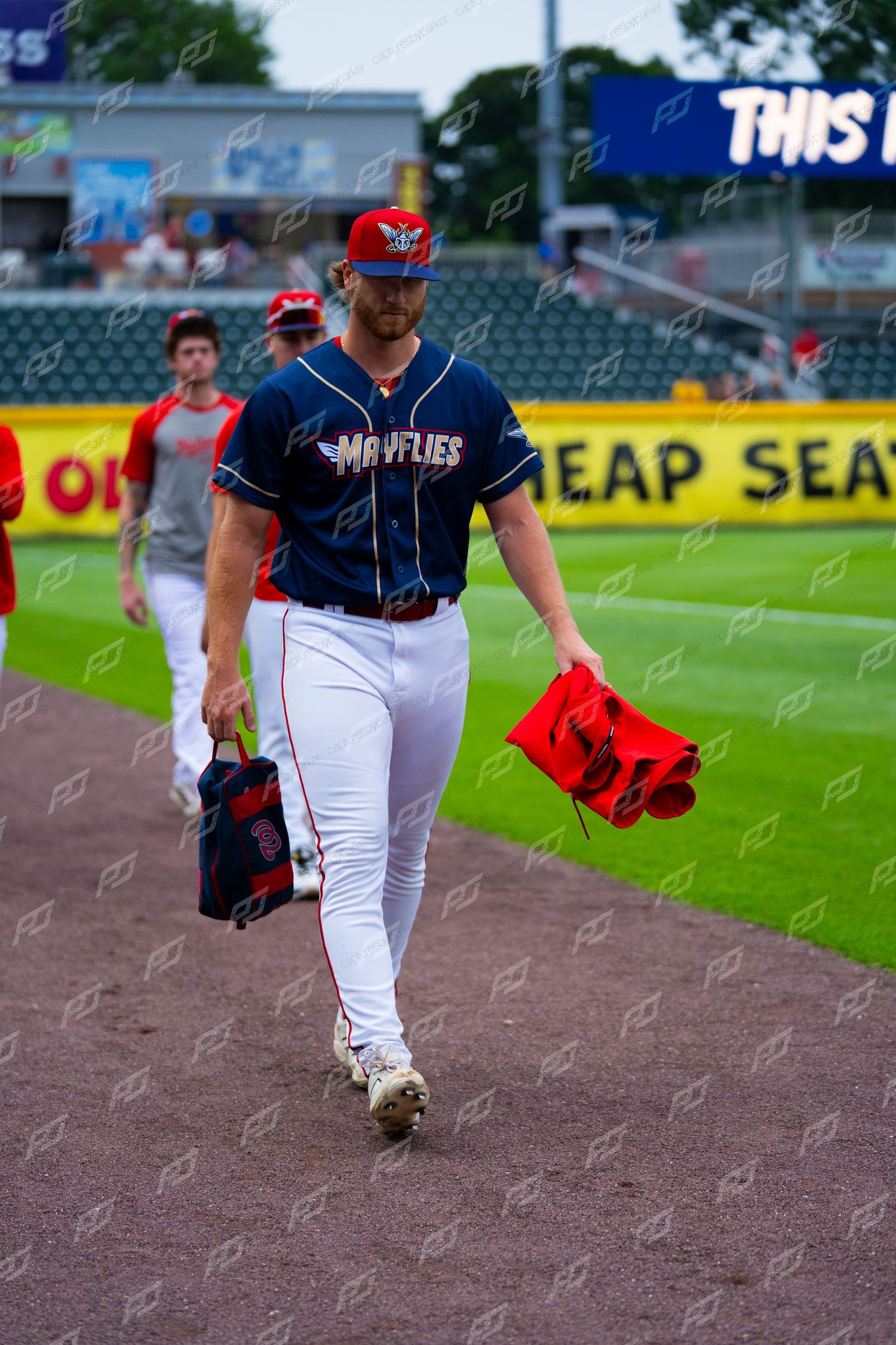 Mayflies minor league baseball player carrying gear while walking along the field warning track.