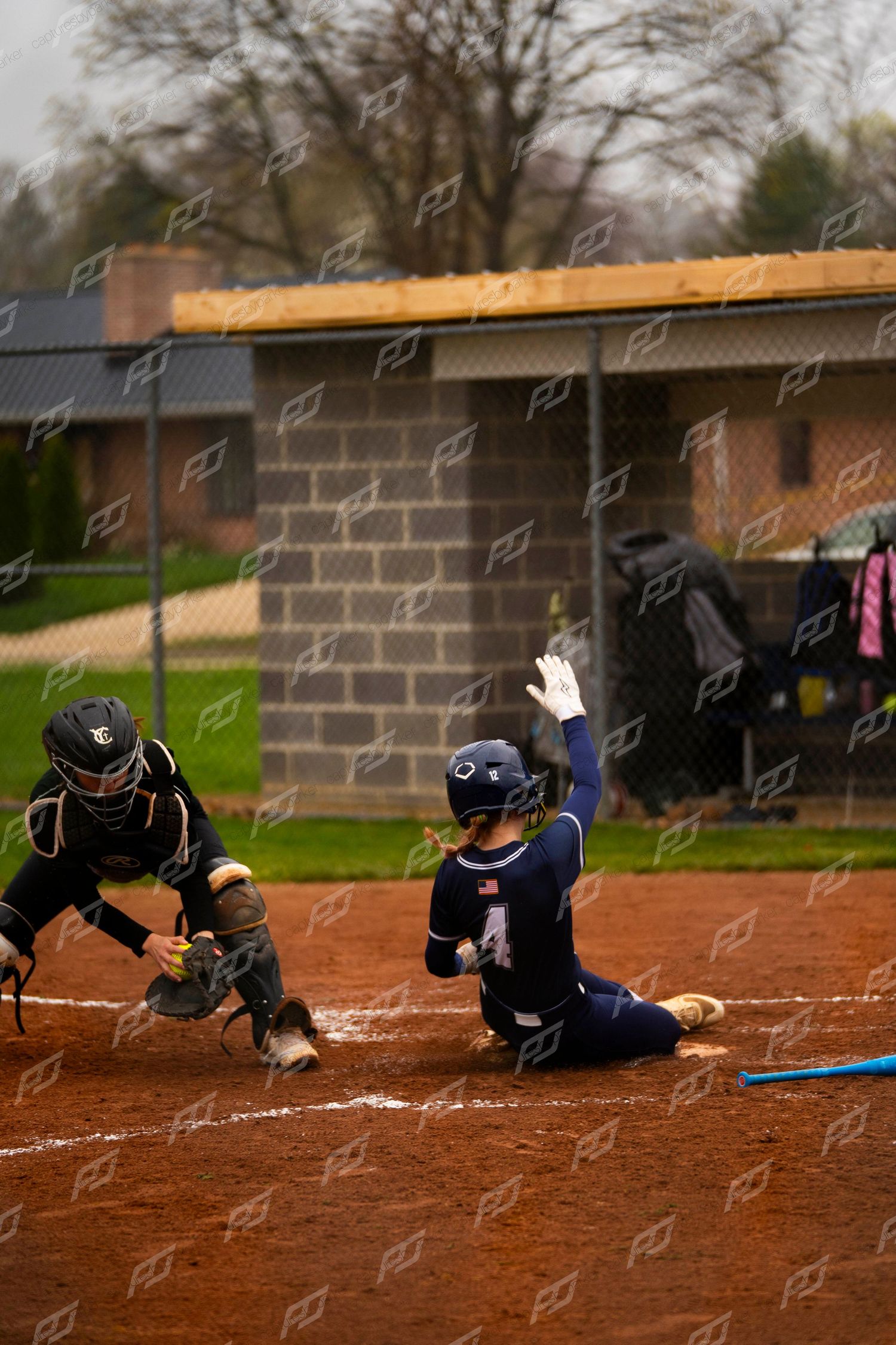 Female softball player #4 slides into home plate as catcher attempts the tag during a softball game.