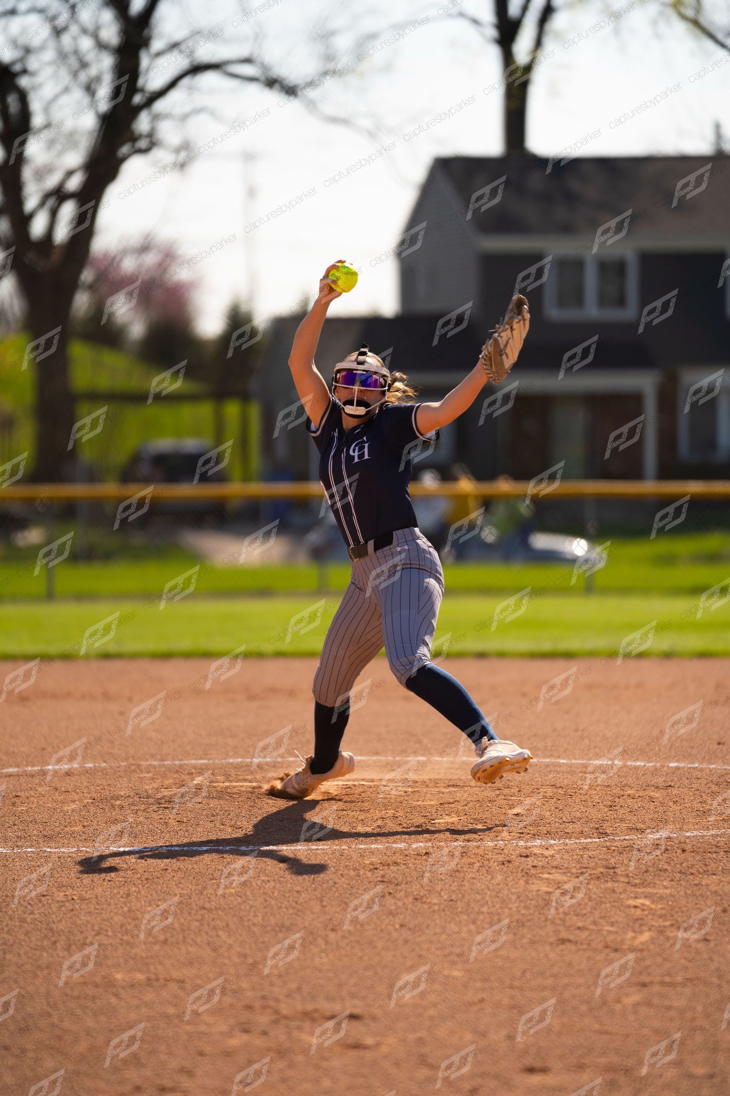 Softball pitcher in navy uniform raises ball overhead preparing to deliver a pitch.