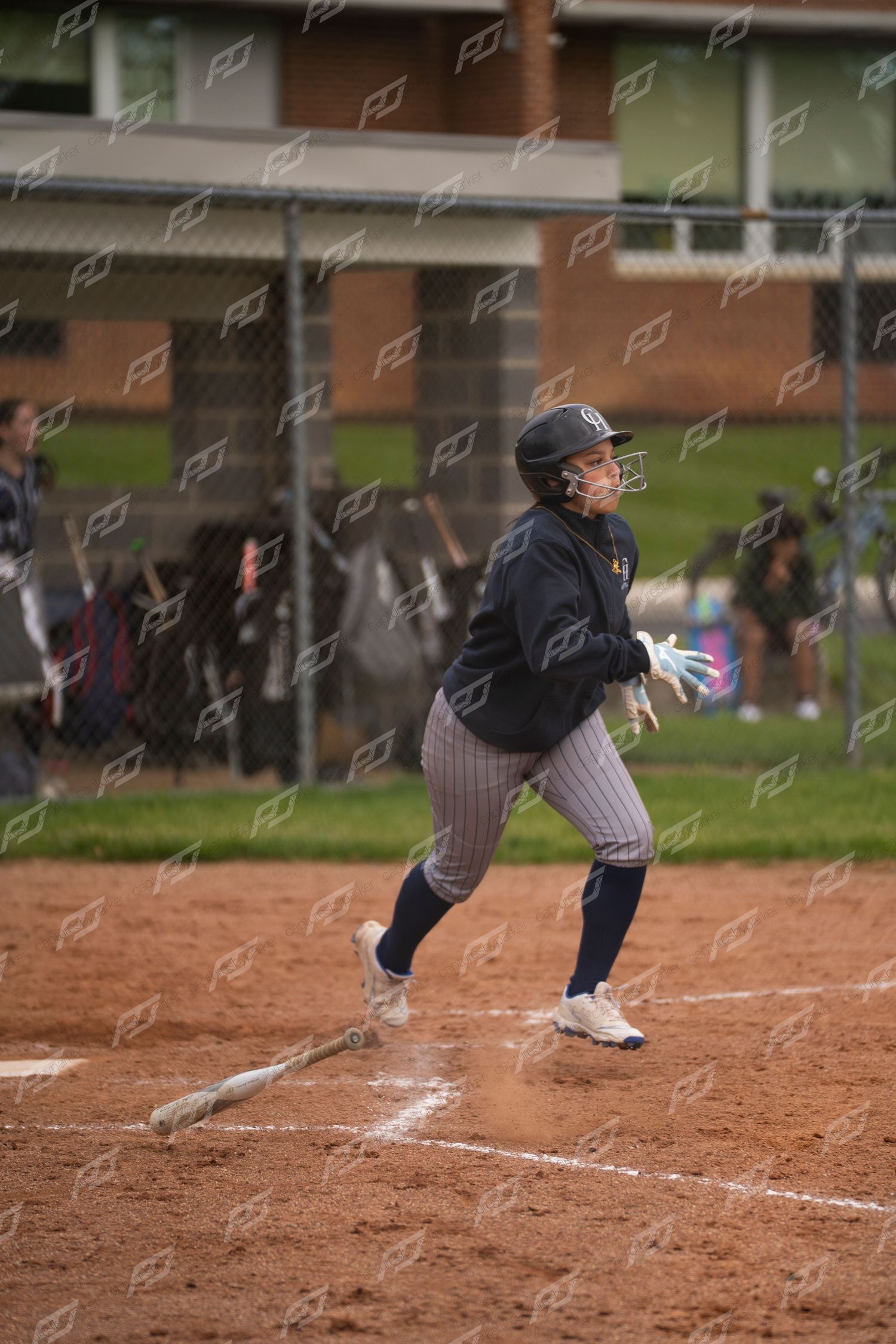 Softball player drops bat and sprints from home plate in navy pinstripe uniform.