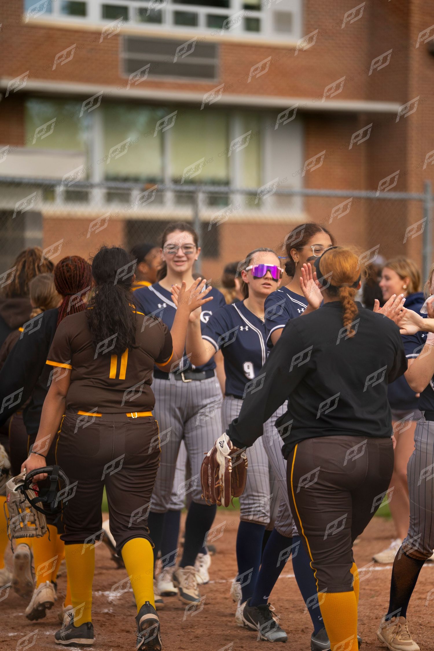 Softball players in navy and brown uniforms exchange high-fives after a game.
