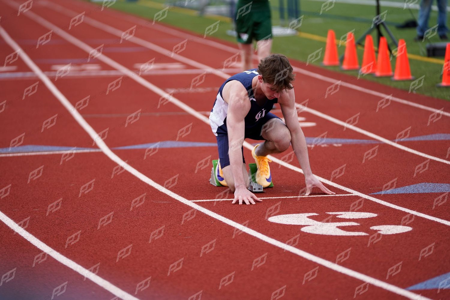 Male track athlete crouches in starting position on red outdoor track preparing for a sprint race.