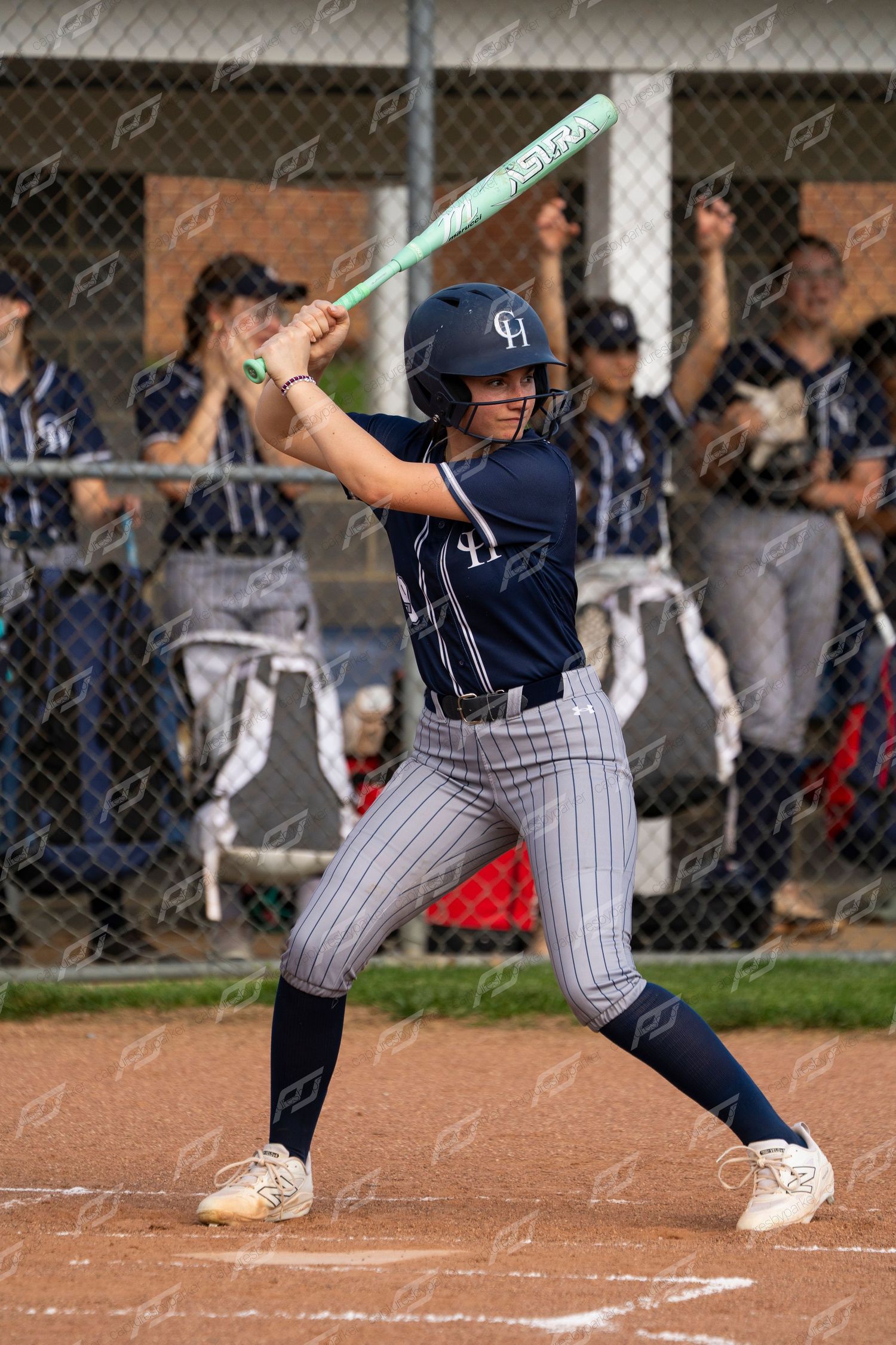 Female batter in CH navy pinstripe uniform prepares to swing a teal bat at home plate.