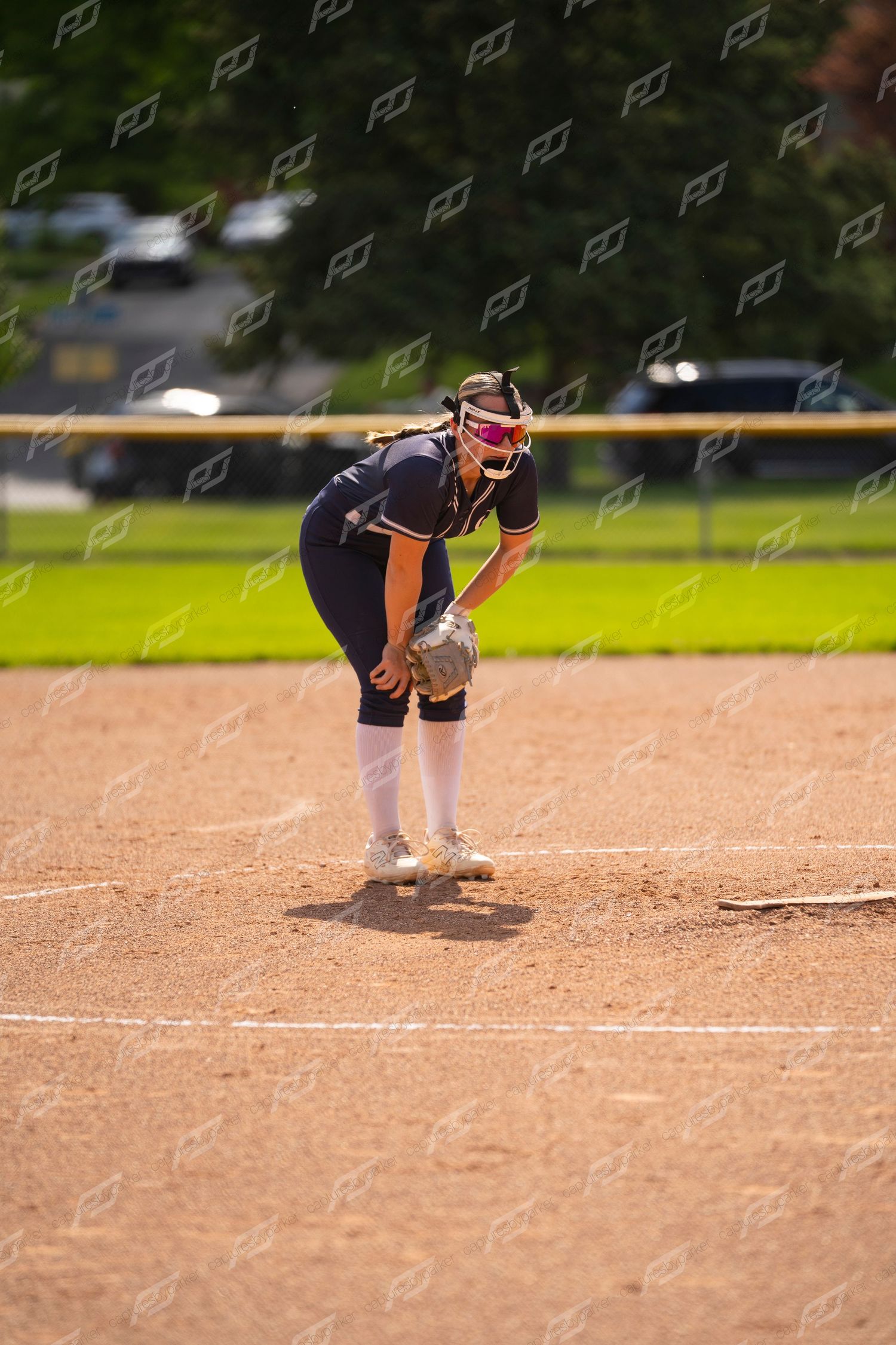 Softball player in navy uniform crouches in ready position on the infield dirt during a game.
