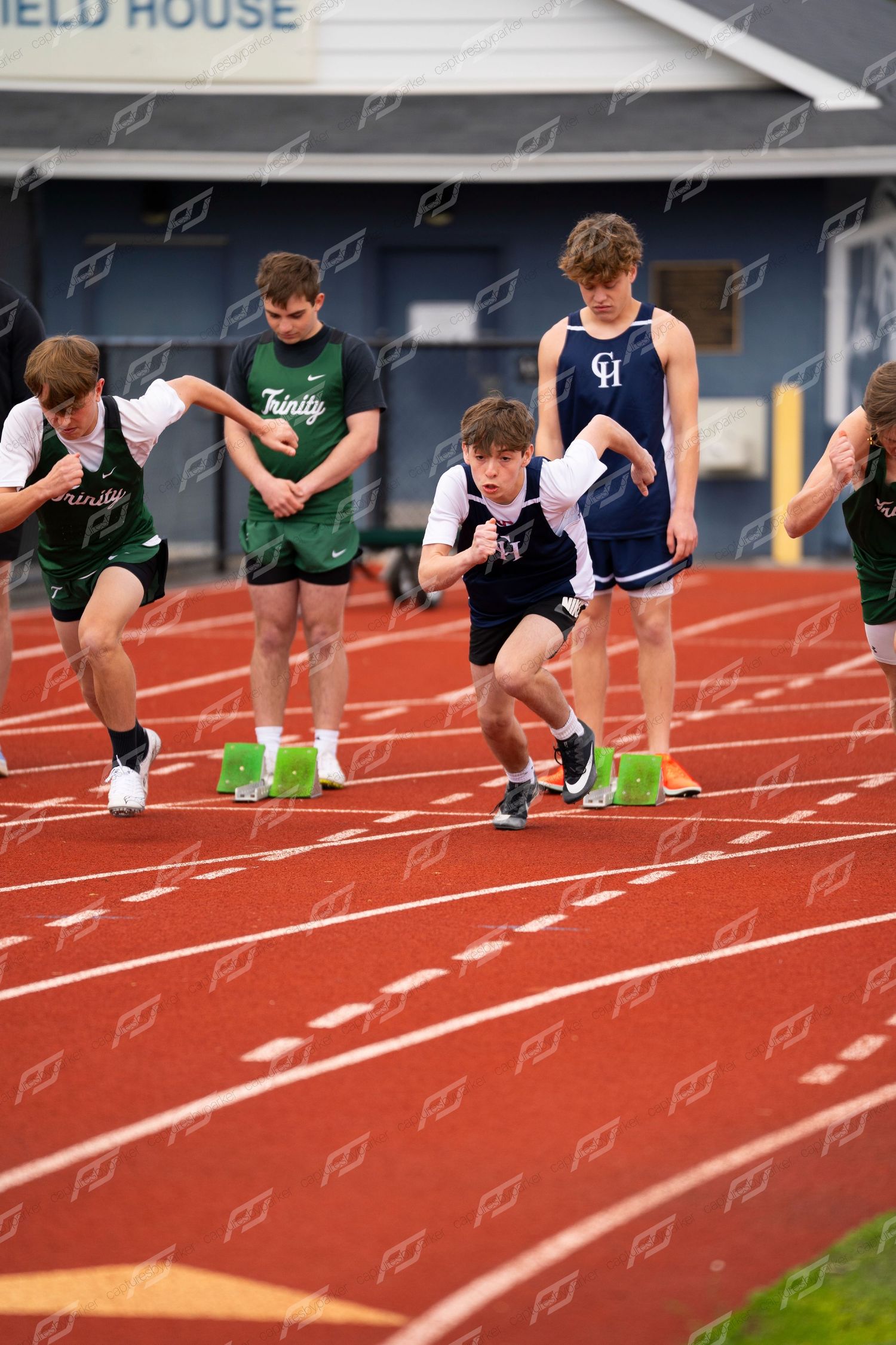 High school sprinters explode from starting blocks at Kunkel Field House track meet with Trinity and CH athletes.