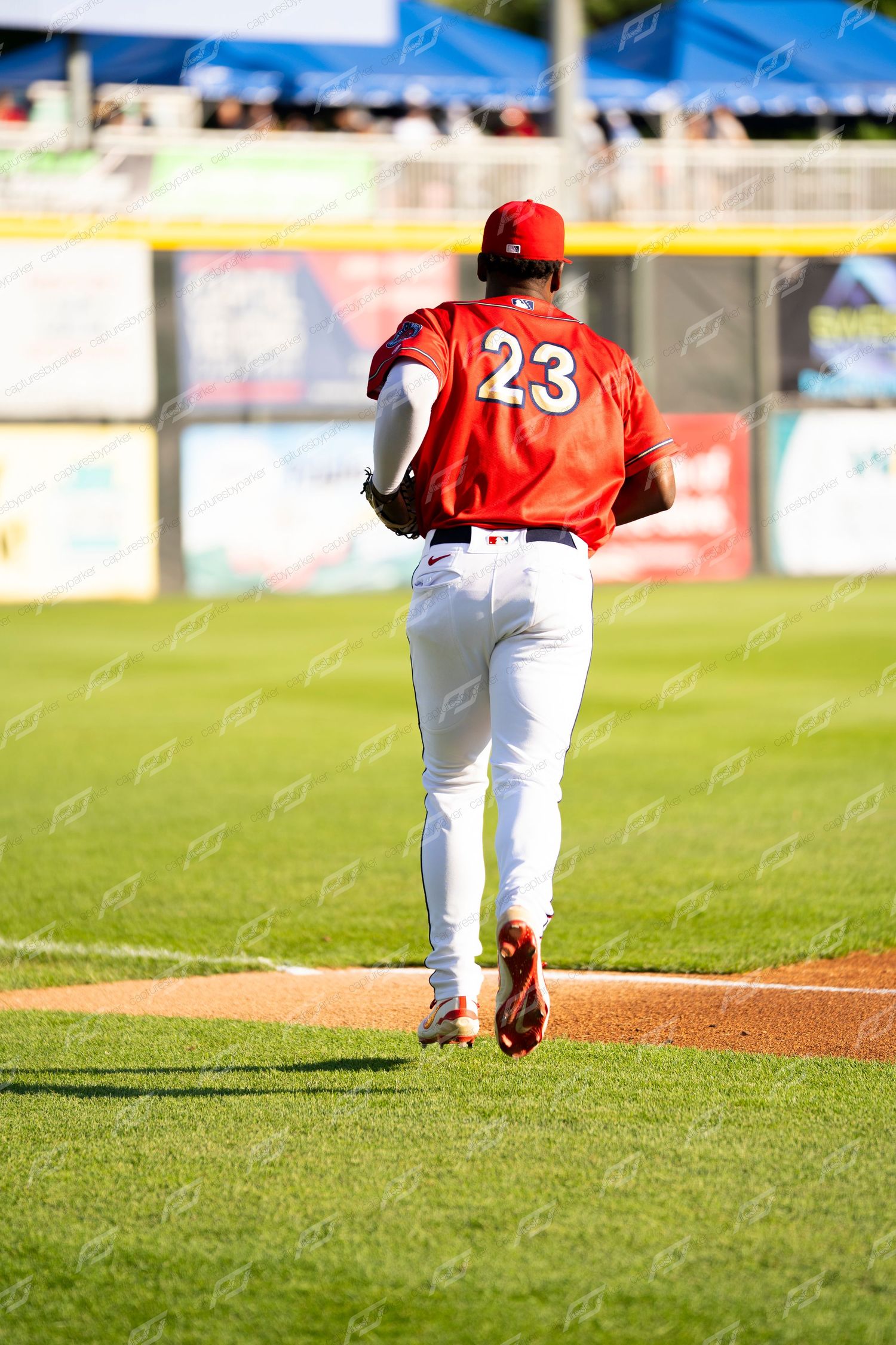 Baseball player #23 in red uniform jogging across the infield dirt during a baseball game.