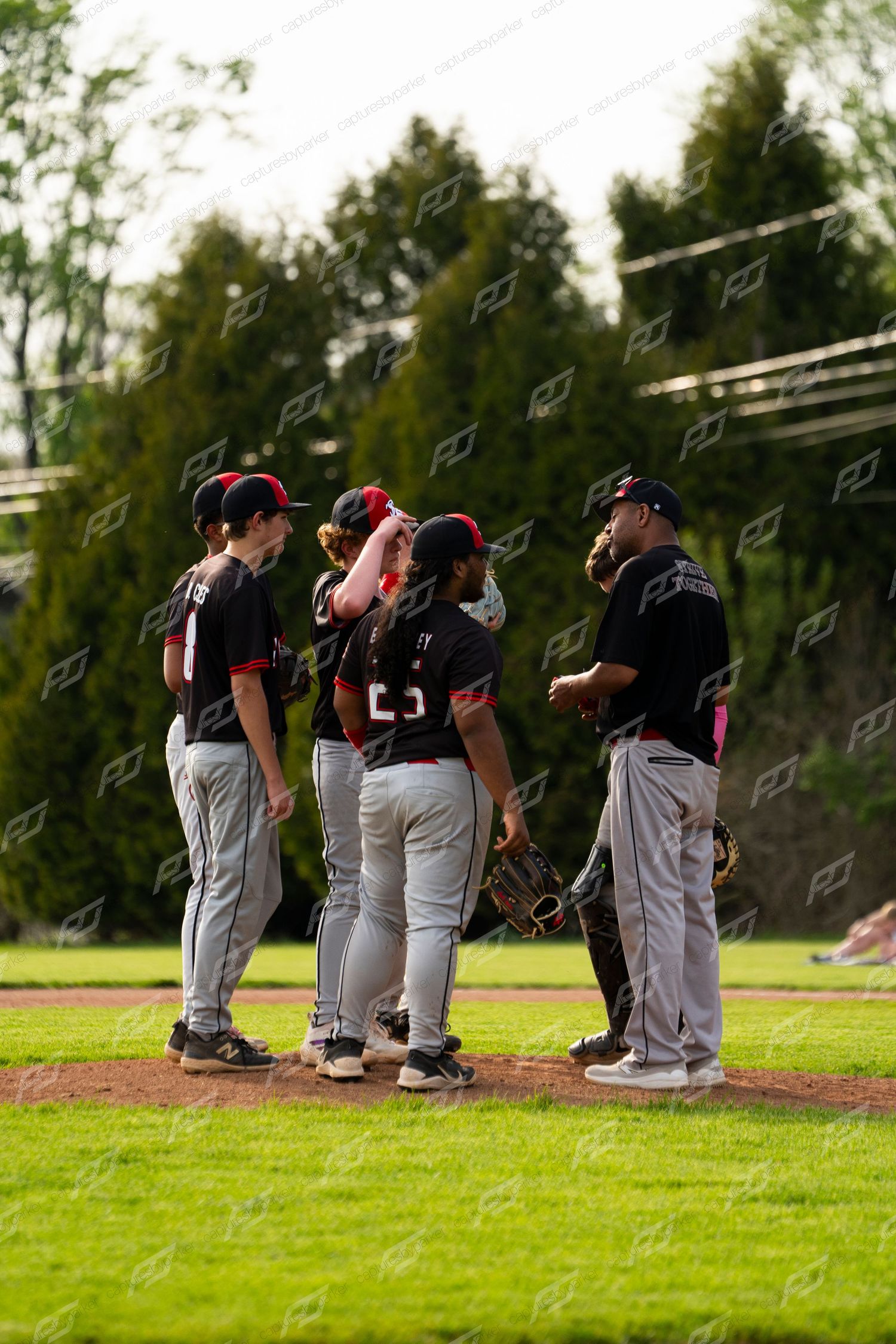 Baseball team in black uniforms huddles on the mound for a pitching change during an outdoor game.