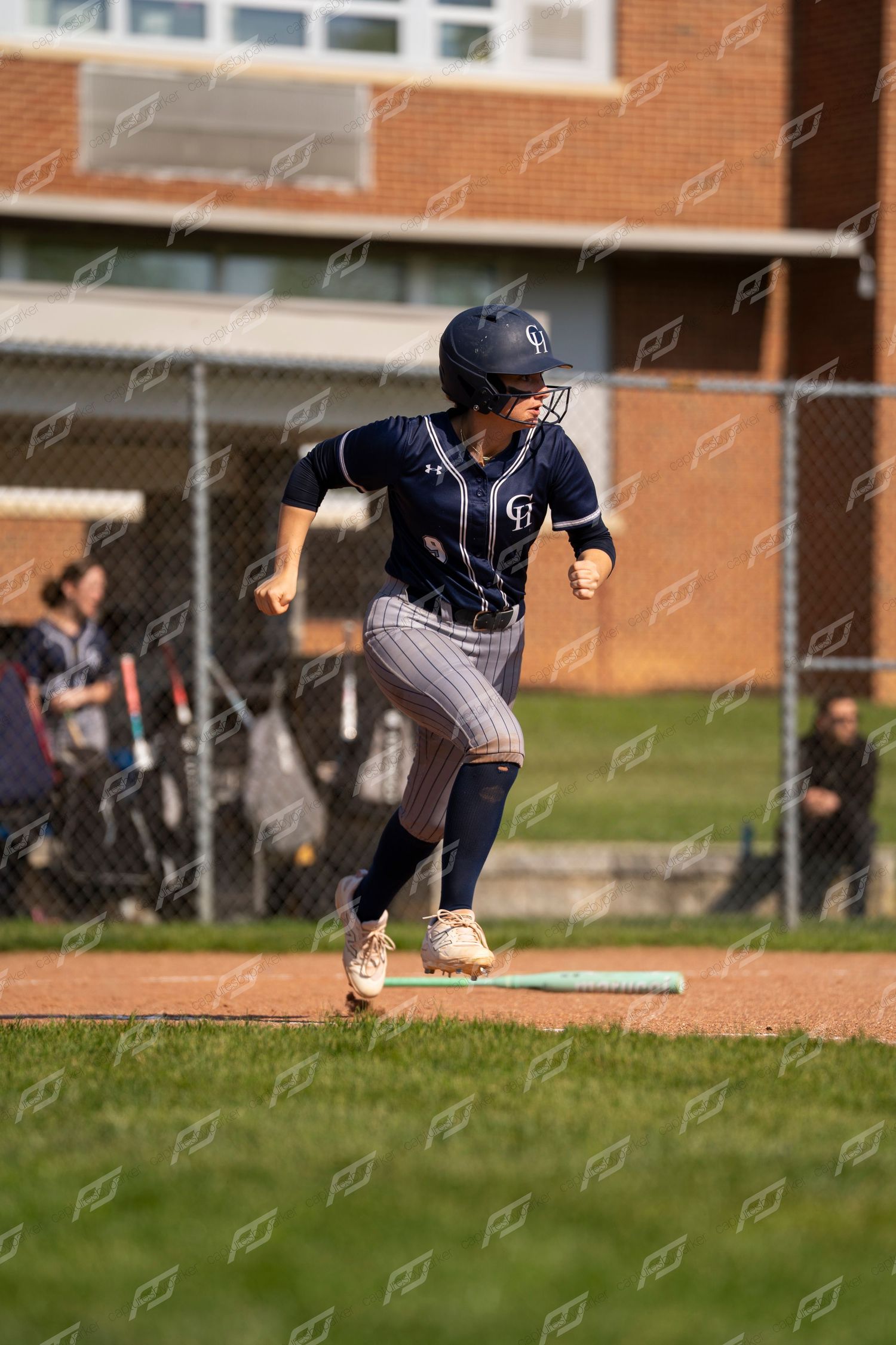Softball player in navy pinstripe uniform sprints from home plate after making contact during a youth softball game.