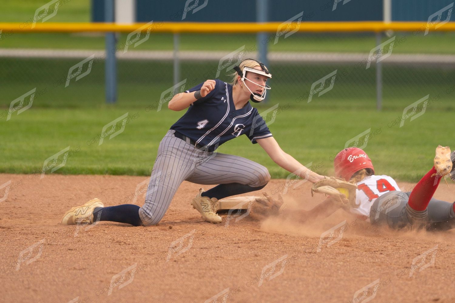 Softball fielder tags out sliding runner at second base during an intense game play.