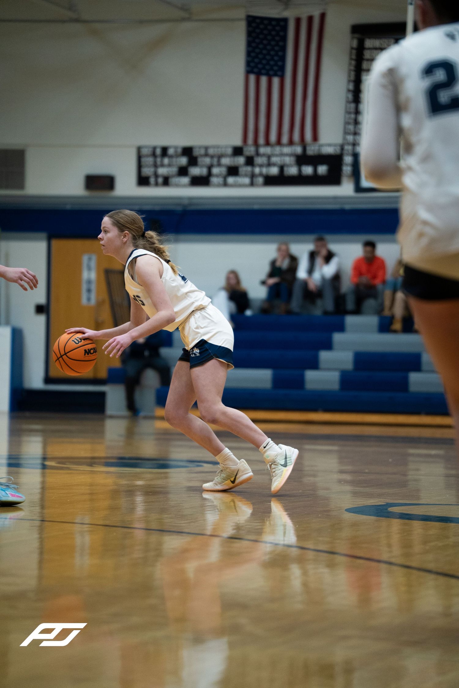 Female Lions basketball player dribbles upcourt during a high school girls basketball game in a blue gymnasium.