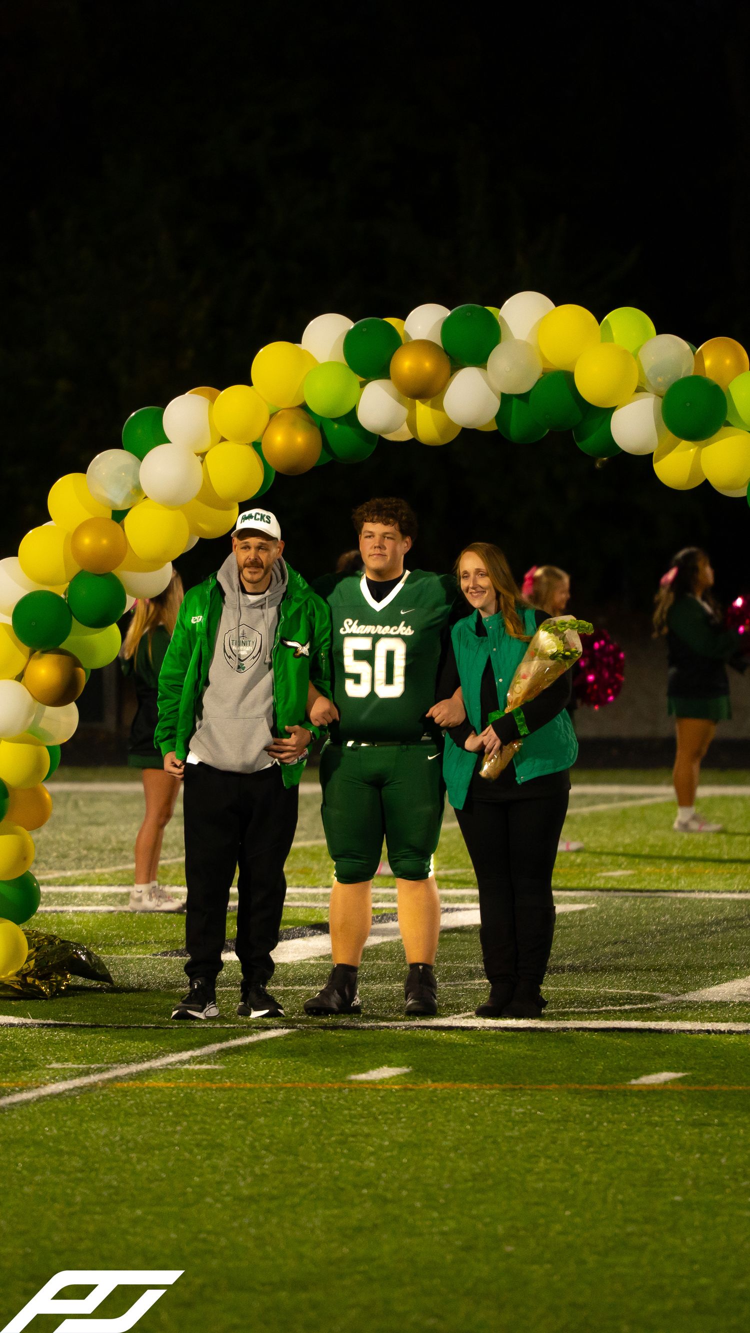 Shamrocks football player #50 walks with two supporters under balloon arch during senior night recognition.