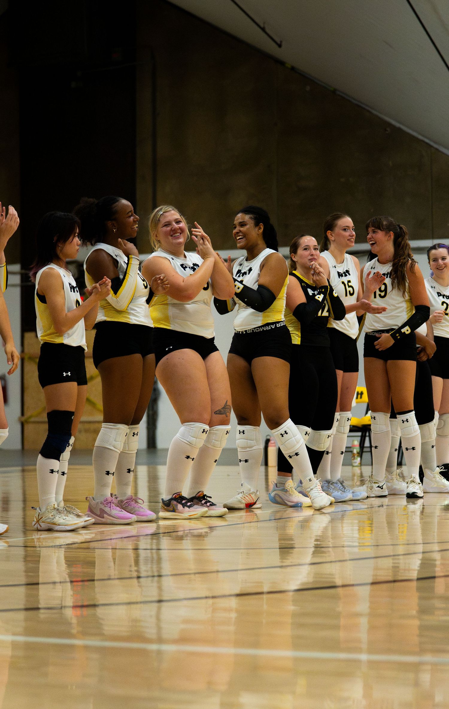 Volleyball team in white and yellow uniforms celebrating together on an indoor court during a match.