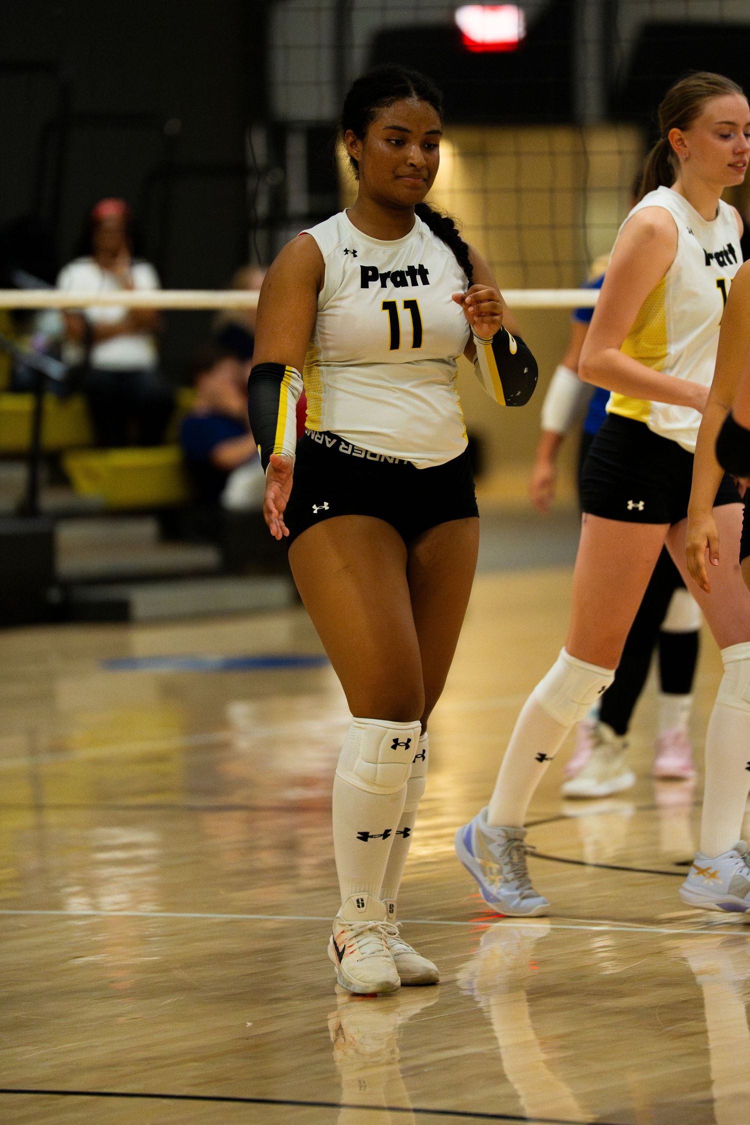 Pratt volleyball player #11 in white and black uniform walks on indoor court during a match.