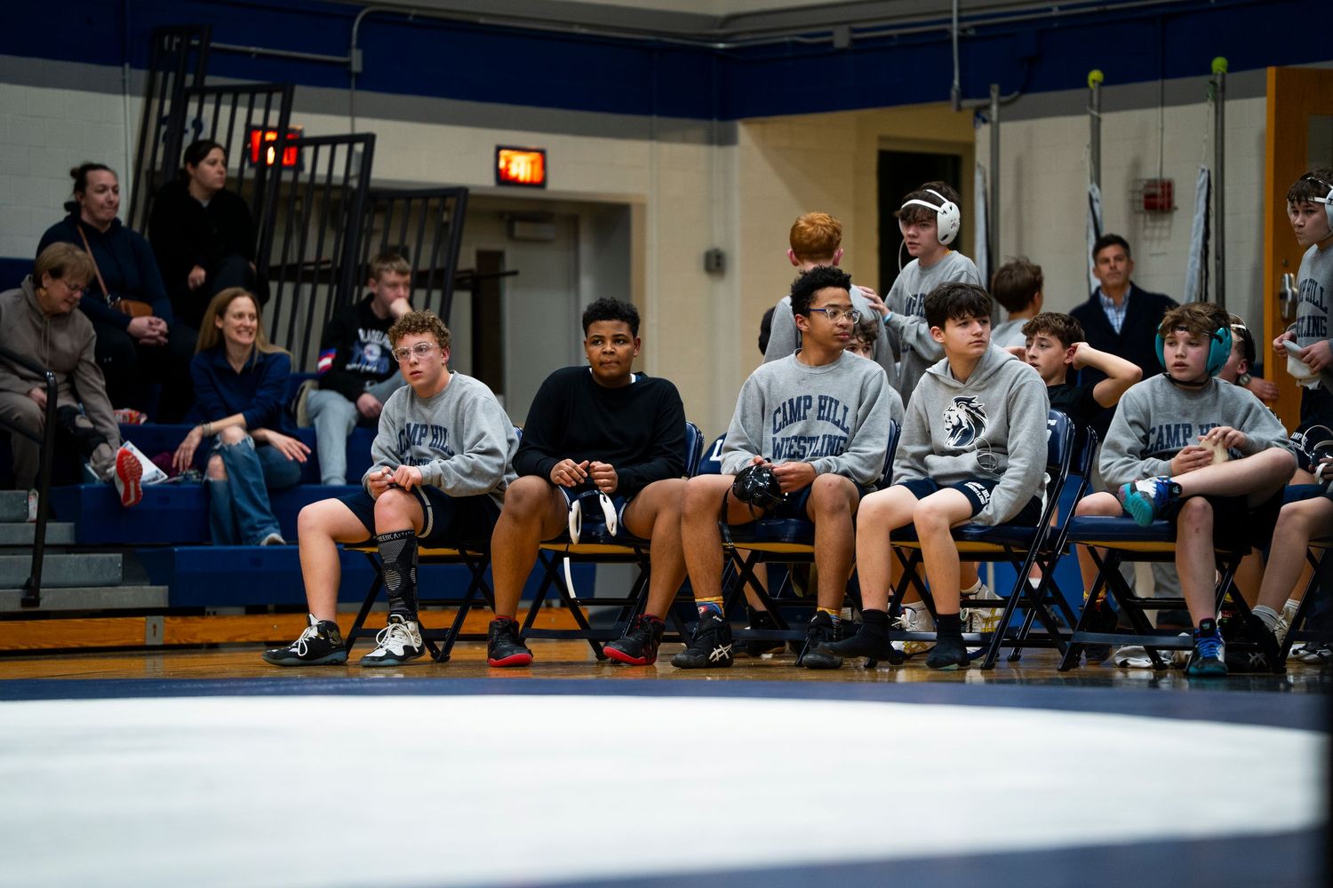 Camp Hill Wrestling team members sit courtside watching teammates compete in a match.