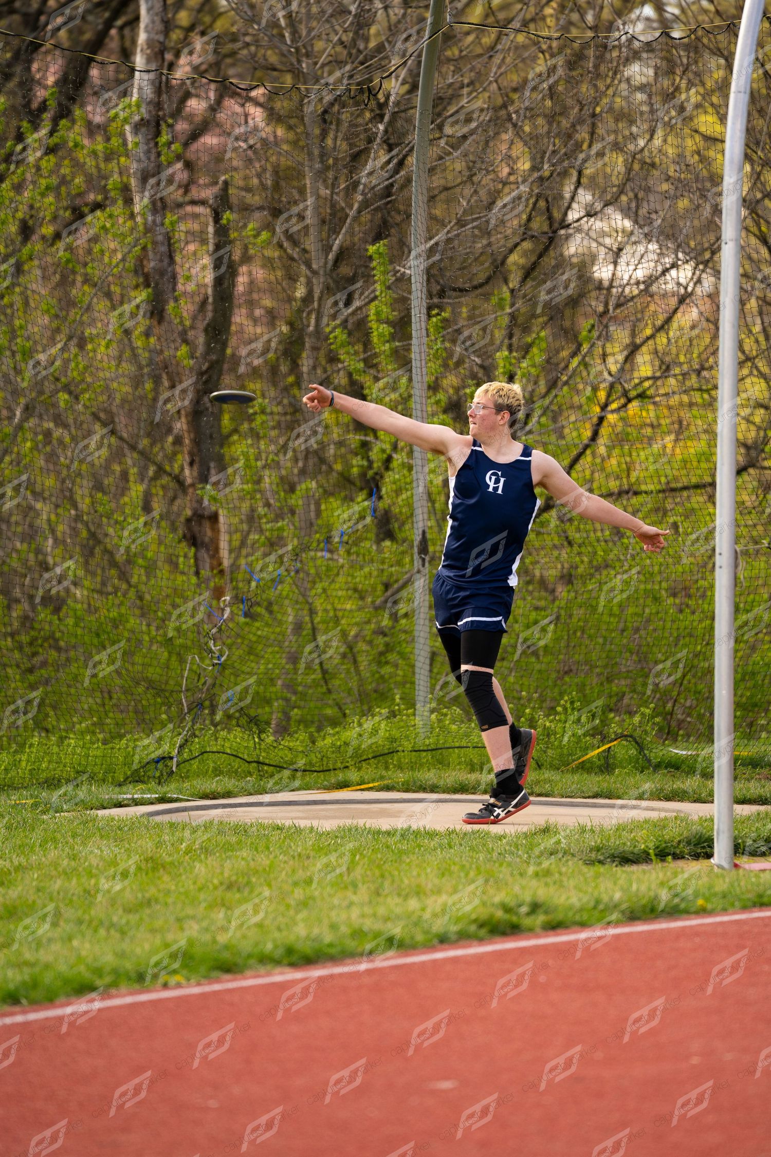 Male discus thrower in navy uniform prepares to release the discus during an outdoor track meet.