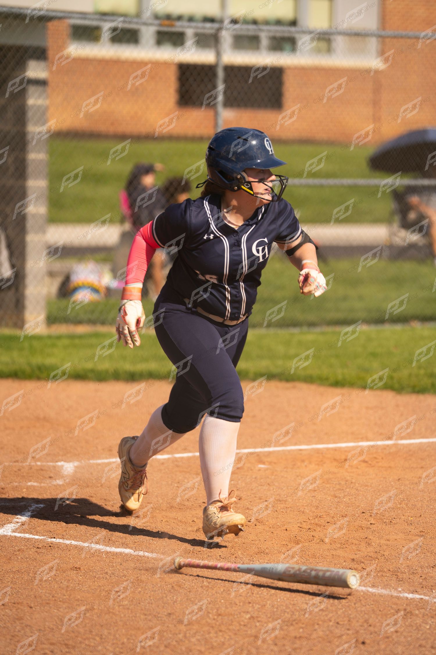 Female softball player in navy uniform running from home plate after dropping the bat.