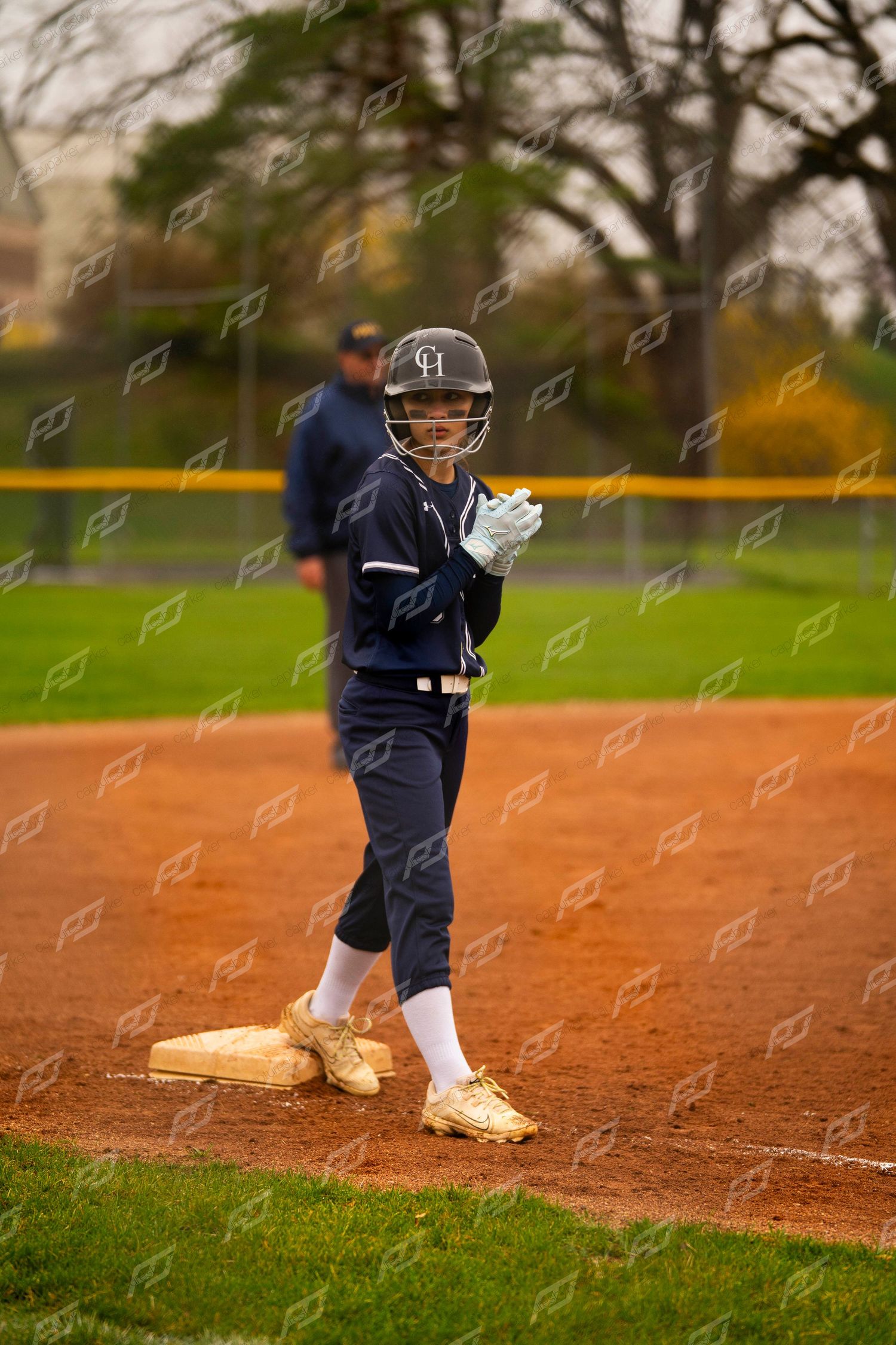 Female softball player stands on first base in navy uniform and gold cleats.