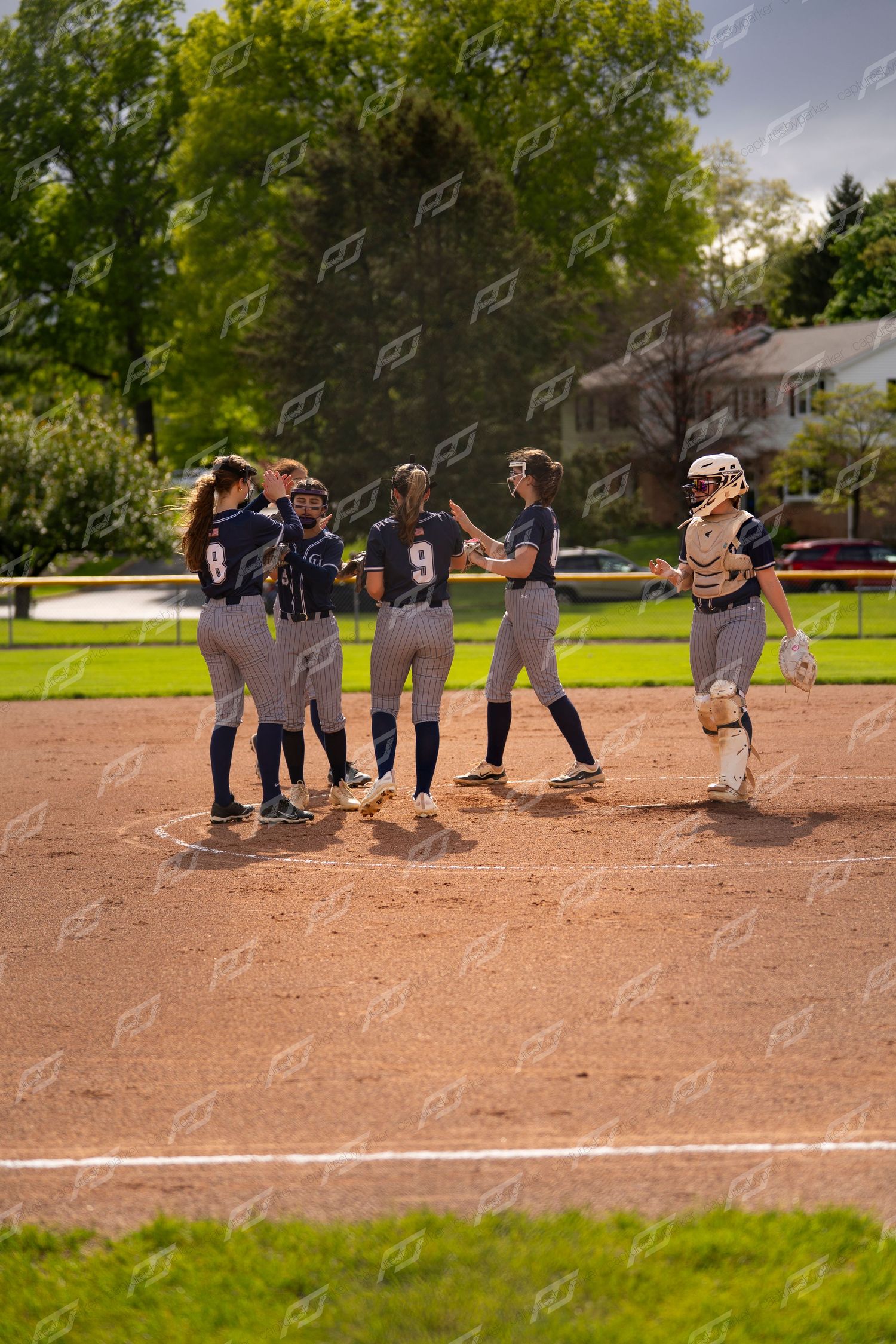 Softball team celebrates together near home plate after scoring a run.