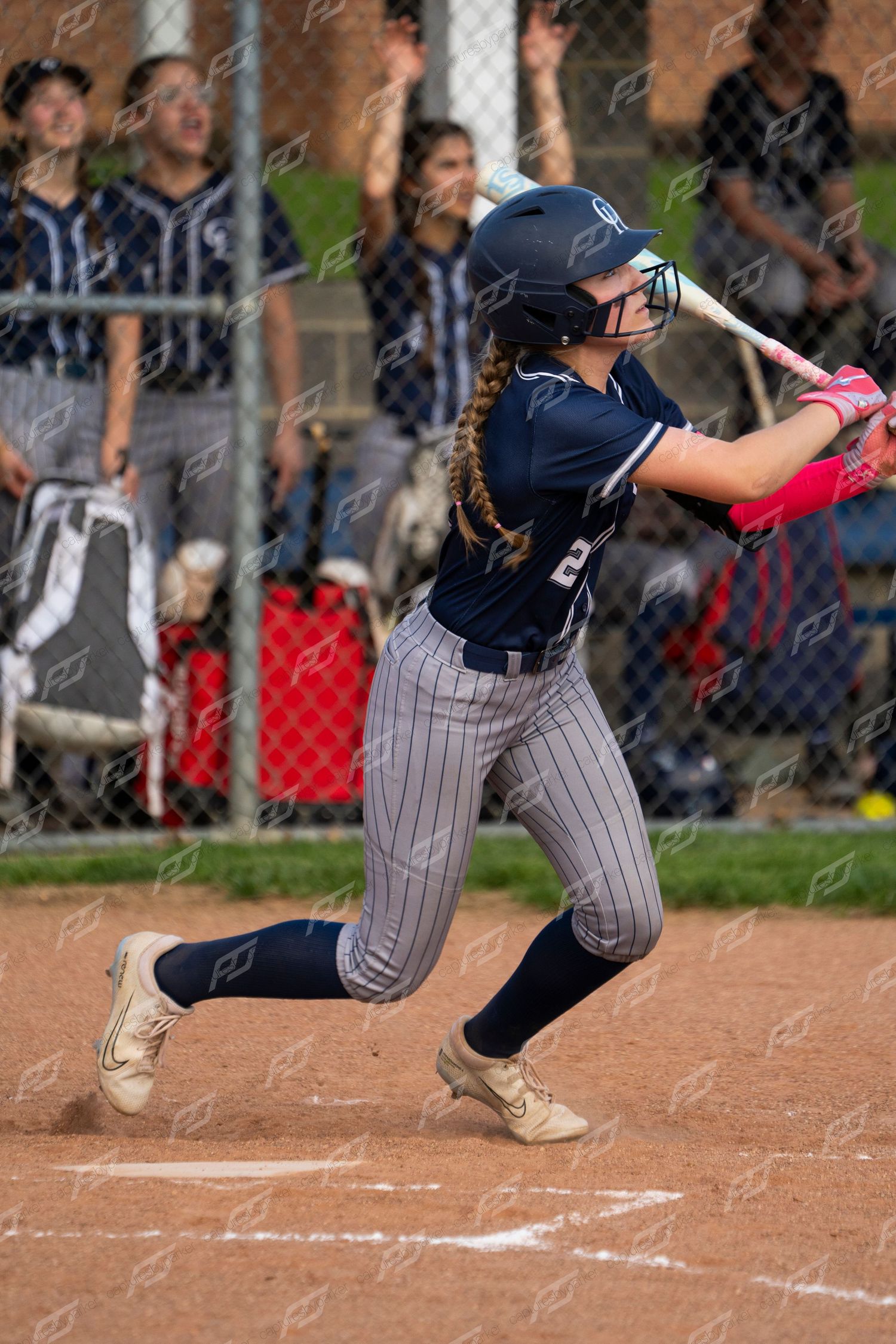 Female softball player in navy pinstripe uniform follows through on bat swing.