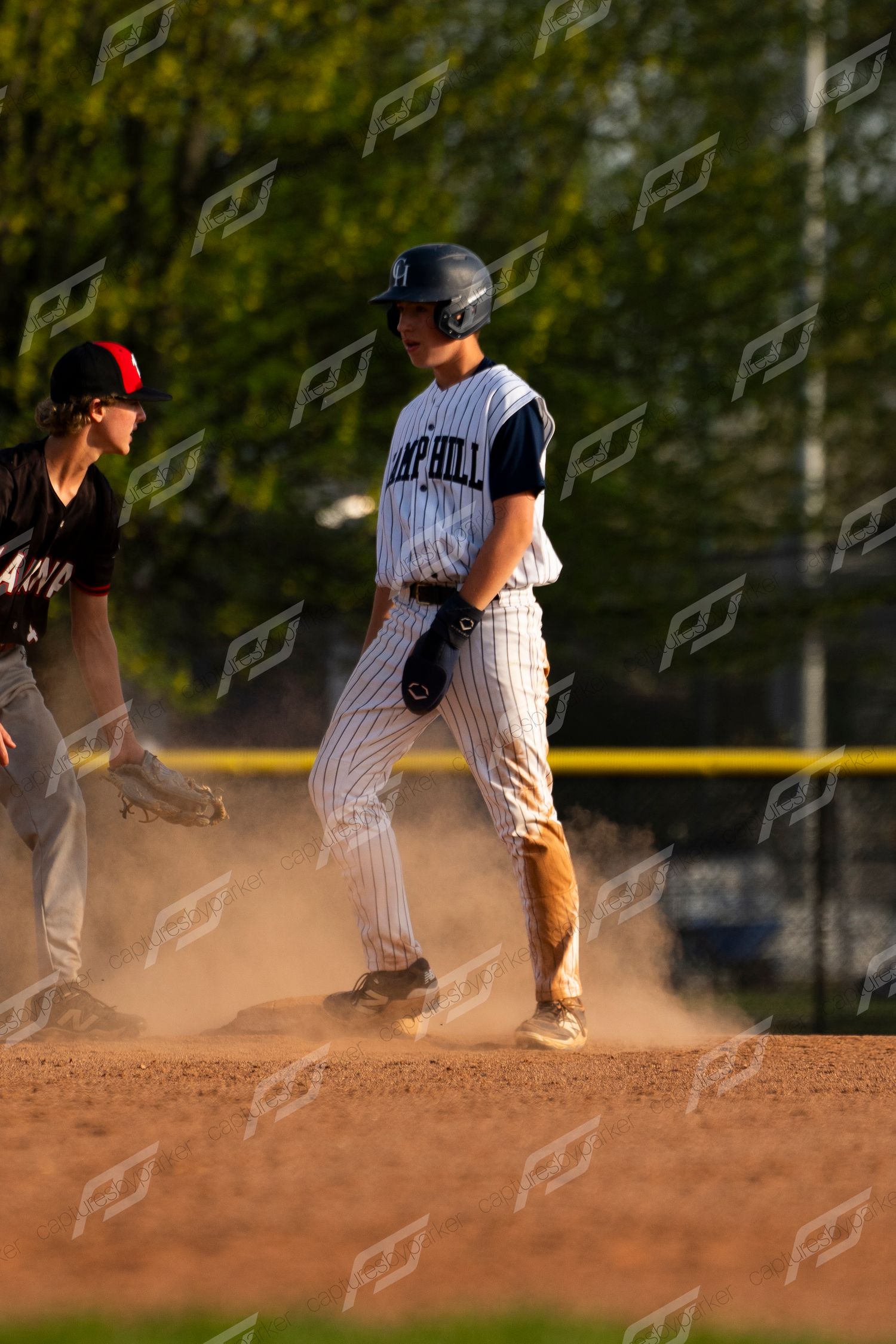 Camp Hill baseball baserunner stands on base in a cloud of dust during a game.