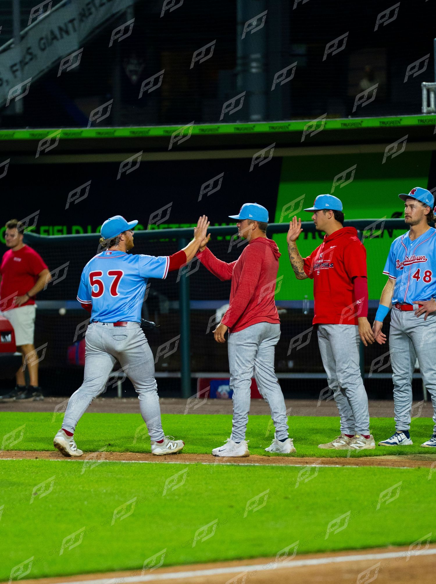 Baseball players exchange high fives near the dugout after a successful play during a night game.