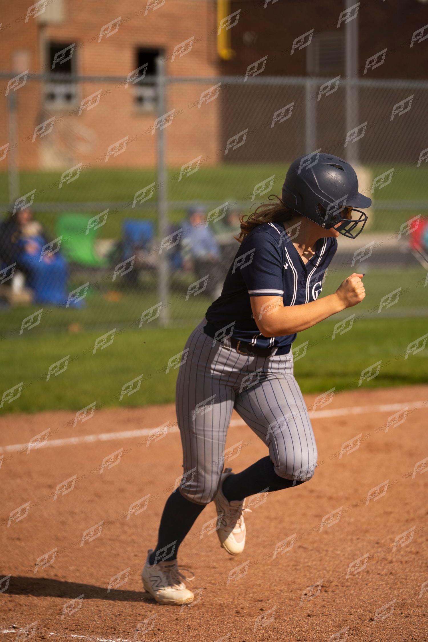 Female softball player in navy uniform runs the bases during a competitive softball game.