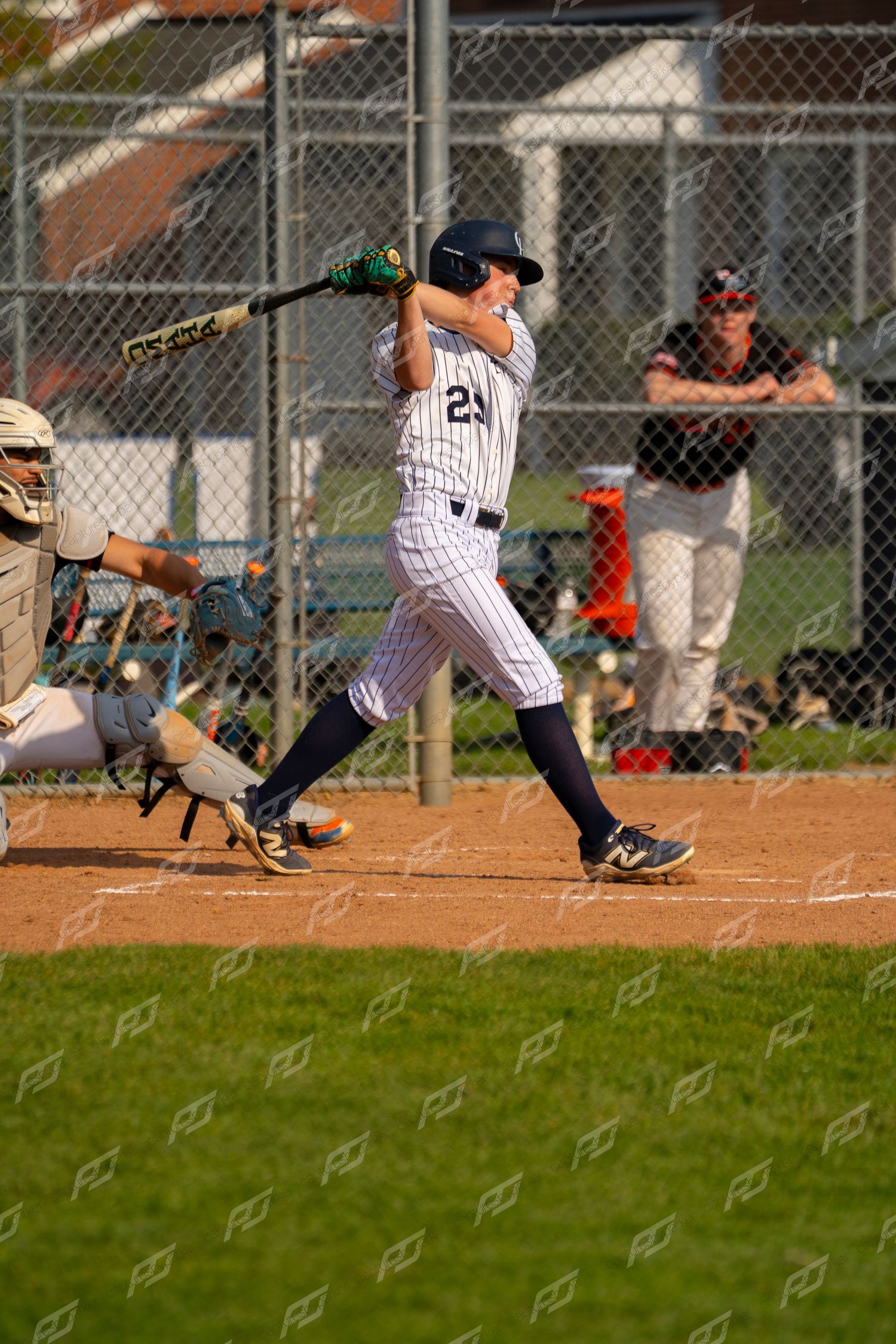 Youth baseball player #25 in white pinstripe uniform swinging bat at home plate.