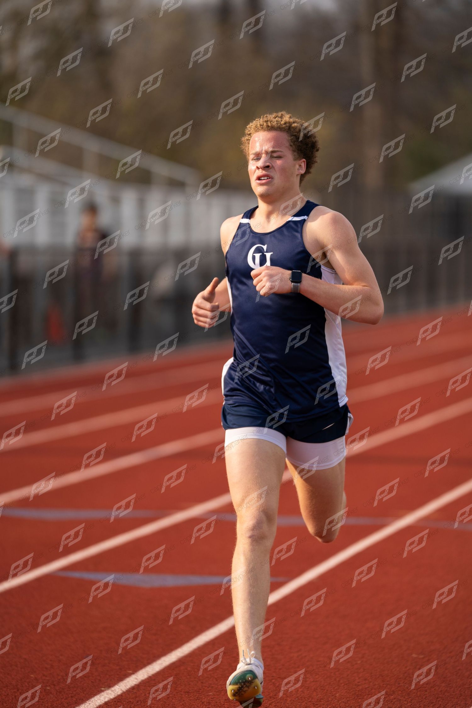 Male CH track runner with curly hair in navy uniform racing on red track.