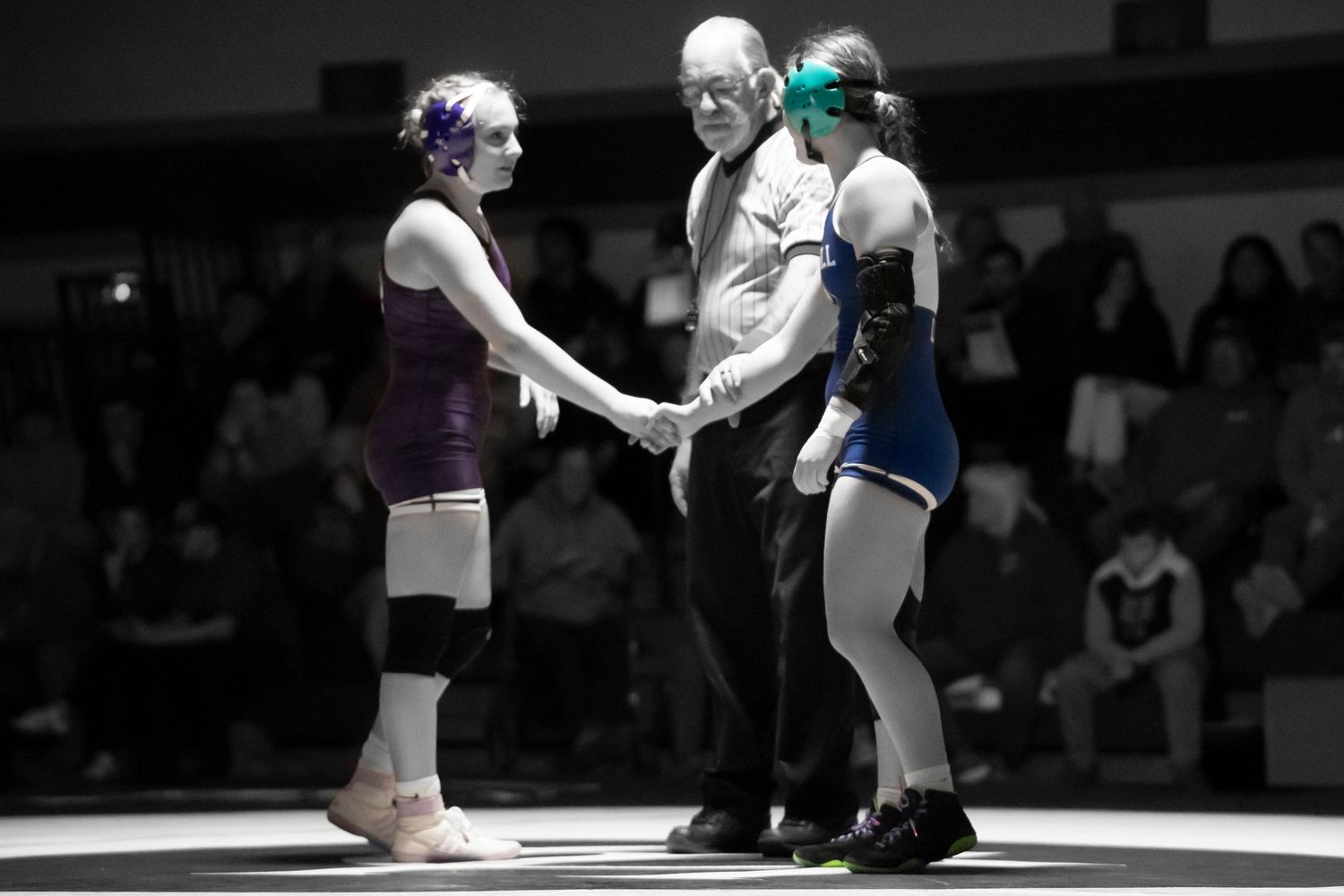 Two female wrestlers shake hands with referee in a black and white wrestling match photo.
