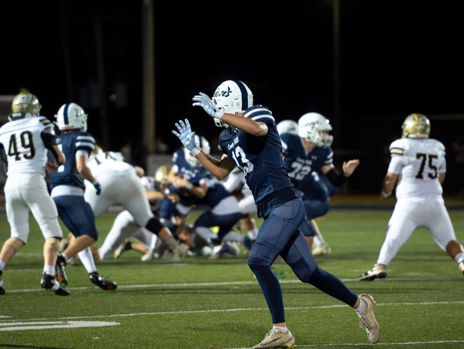 Camp Hill football player catches pass during night game with opponents in gold uniforms nearby.