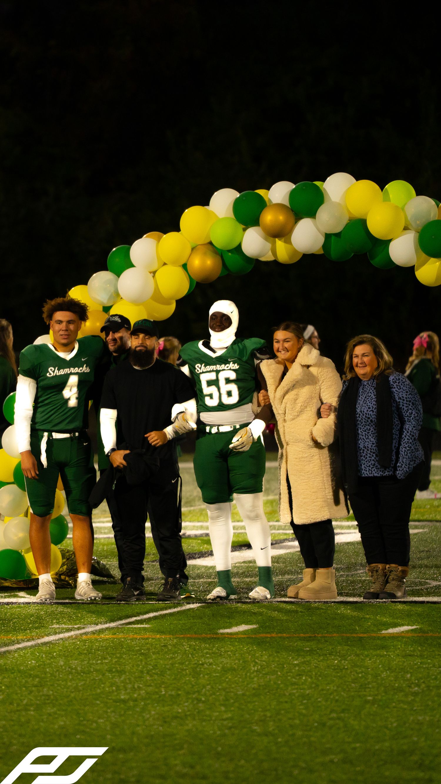Shamrocks football player #56 walks with family under green and yellow balloon arch during senior night.