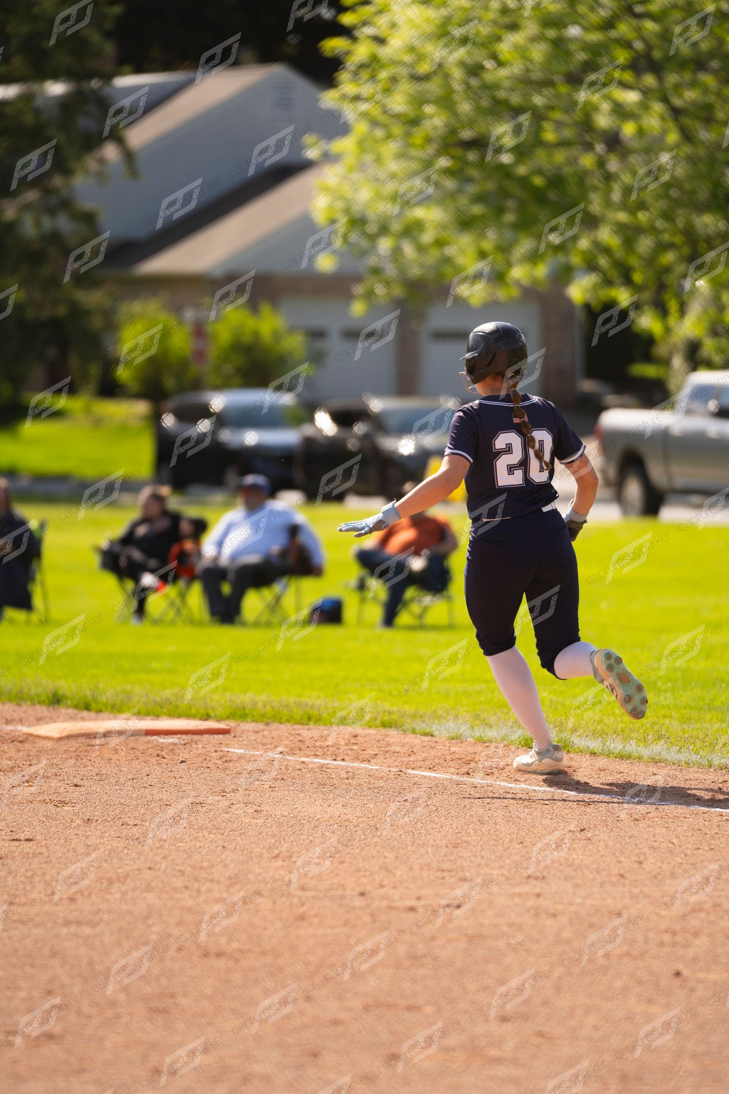 Softball player number 20 in navy uniform runs toward first base during a game.