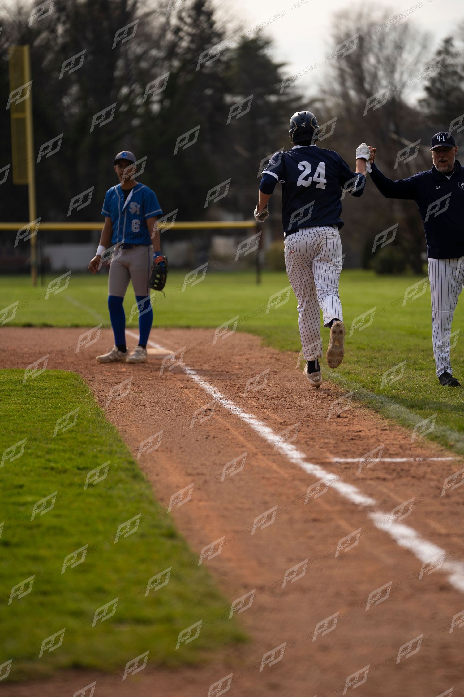 Baseball player #24 runs toward third base coach for high five during game.