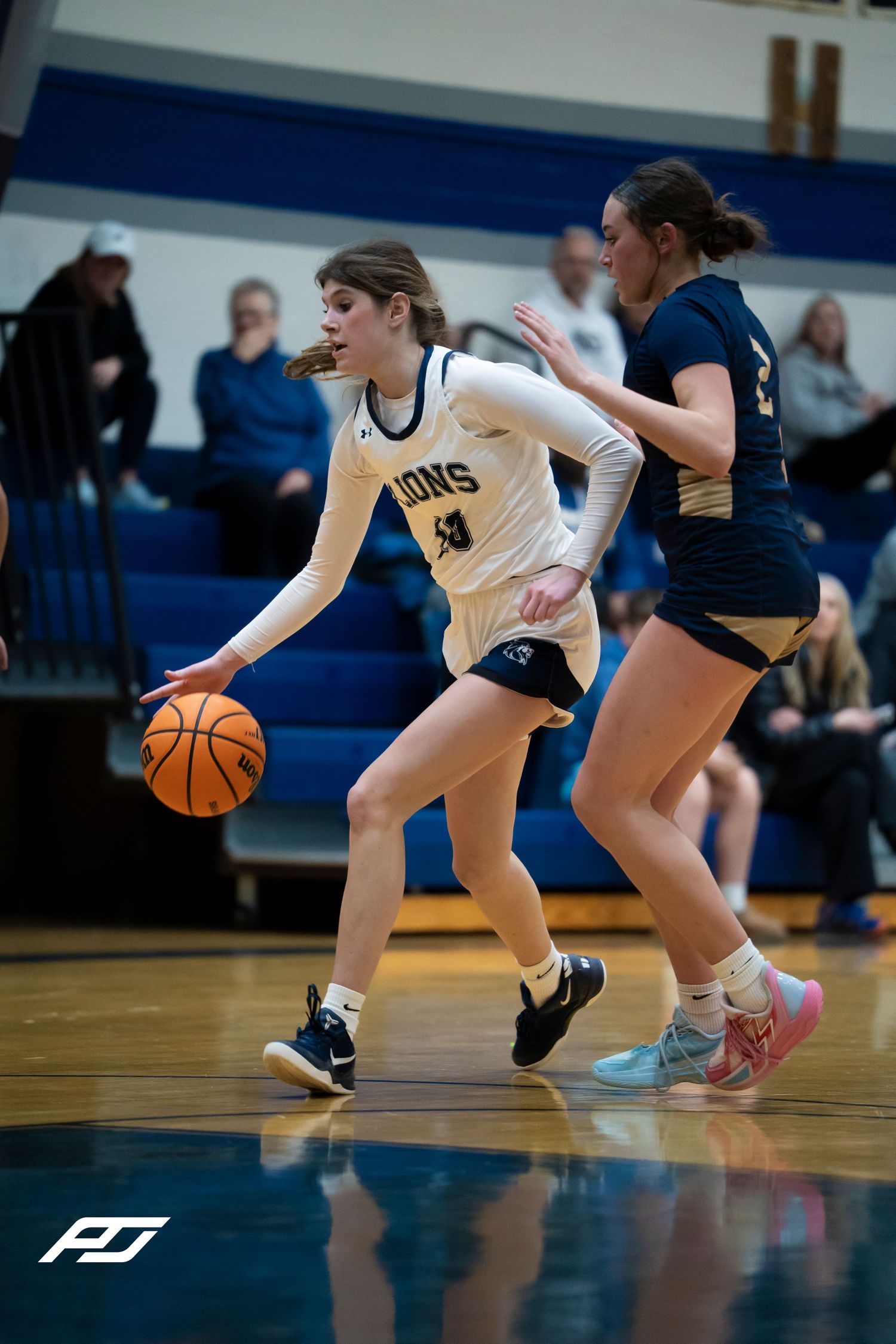 Lions #40 female basketball player drives past a defender during a high school girls basketball game.