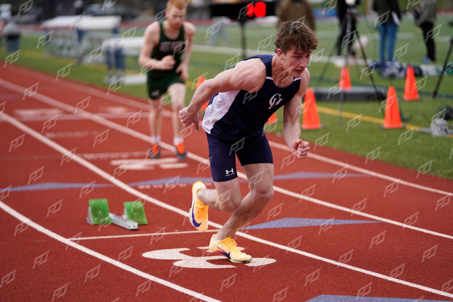 Young male athlete launching from starting blocks during a sprint race on a red track.