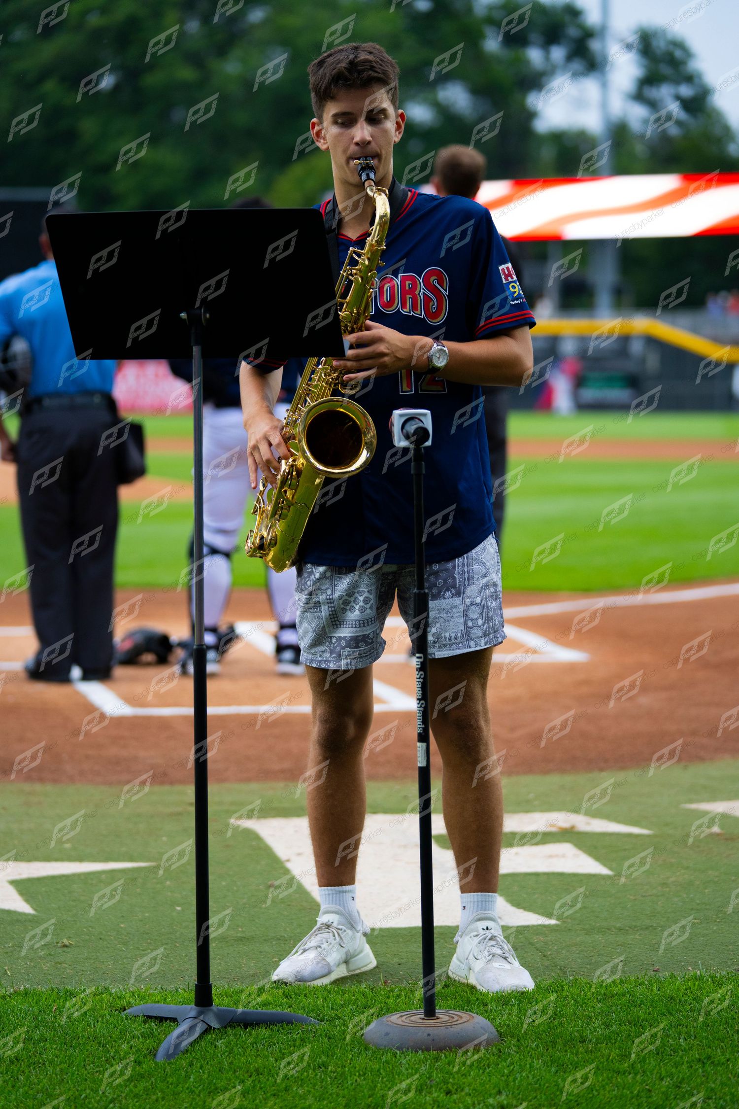 Young man playing saxophone for the national anthem on a baseball field before a minor league game.