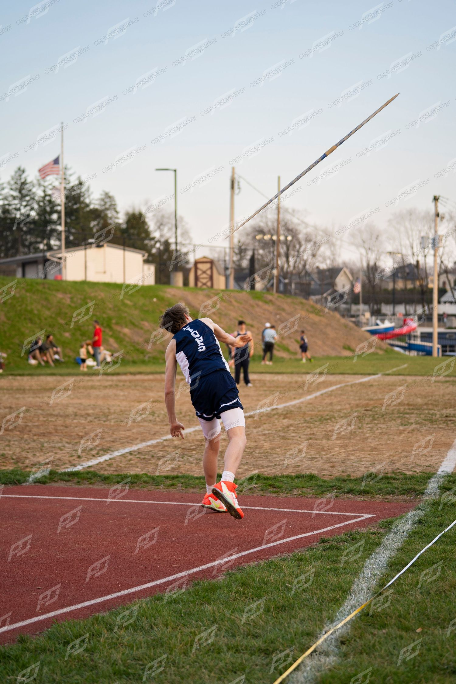 Male athlete in navy uniform after releasing javelin at track meet.