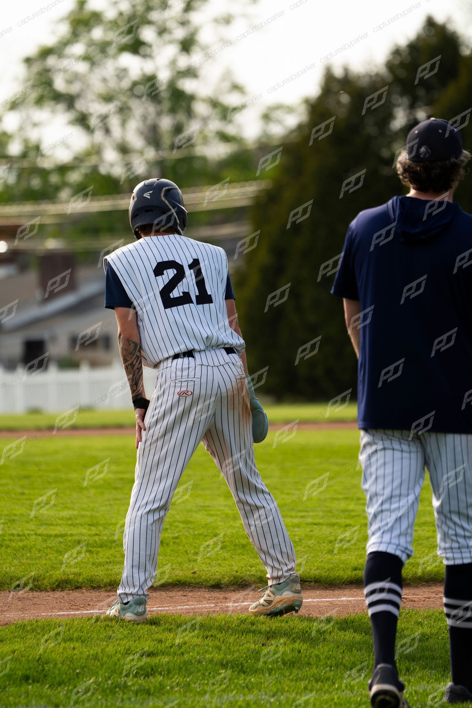 Baseball player number 21 in white pinstripe uniform leads off base during an outdoor evening game.