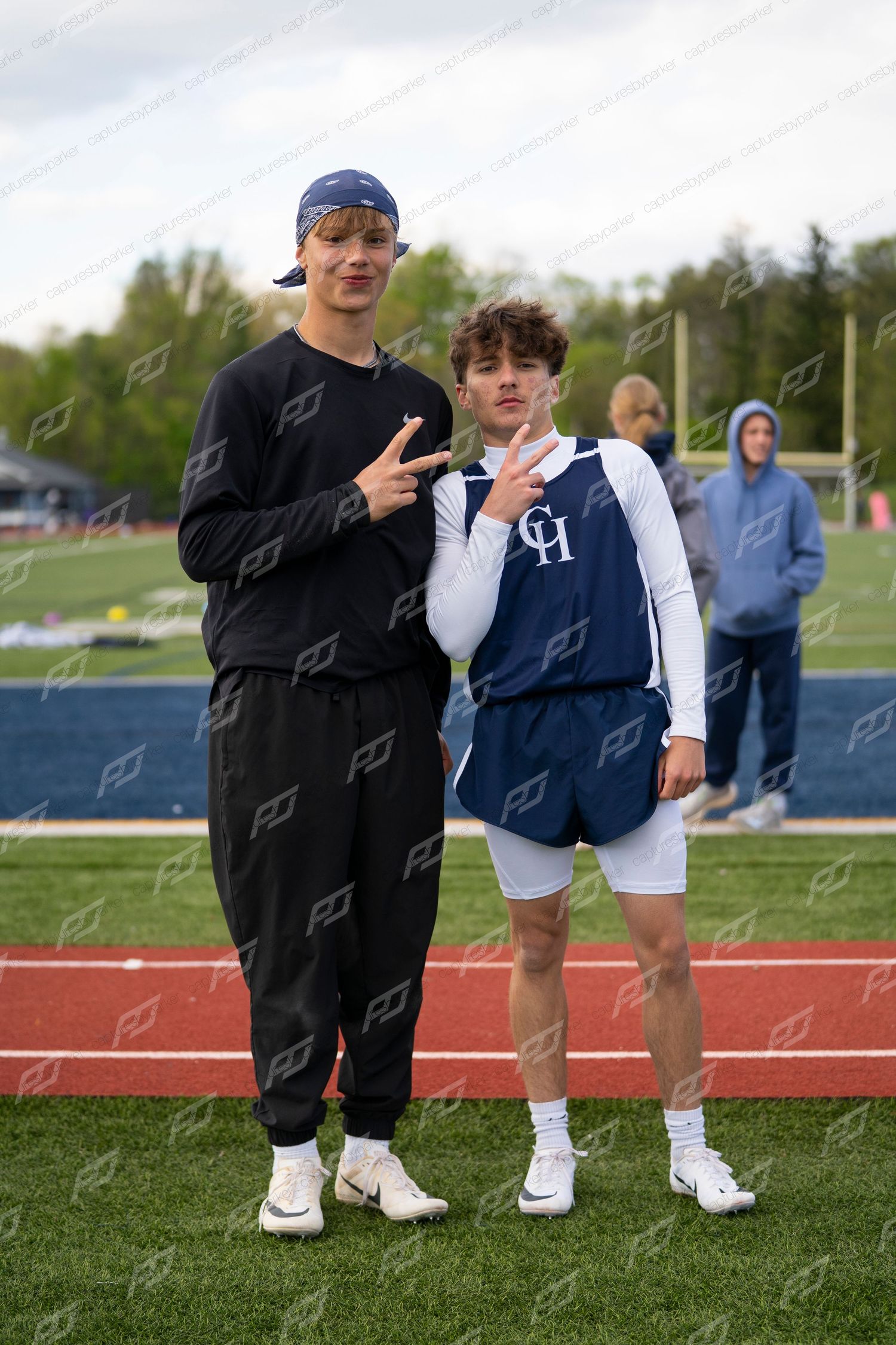 Two young male athletes pose together on a track field giving peace signs.