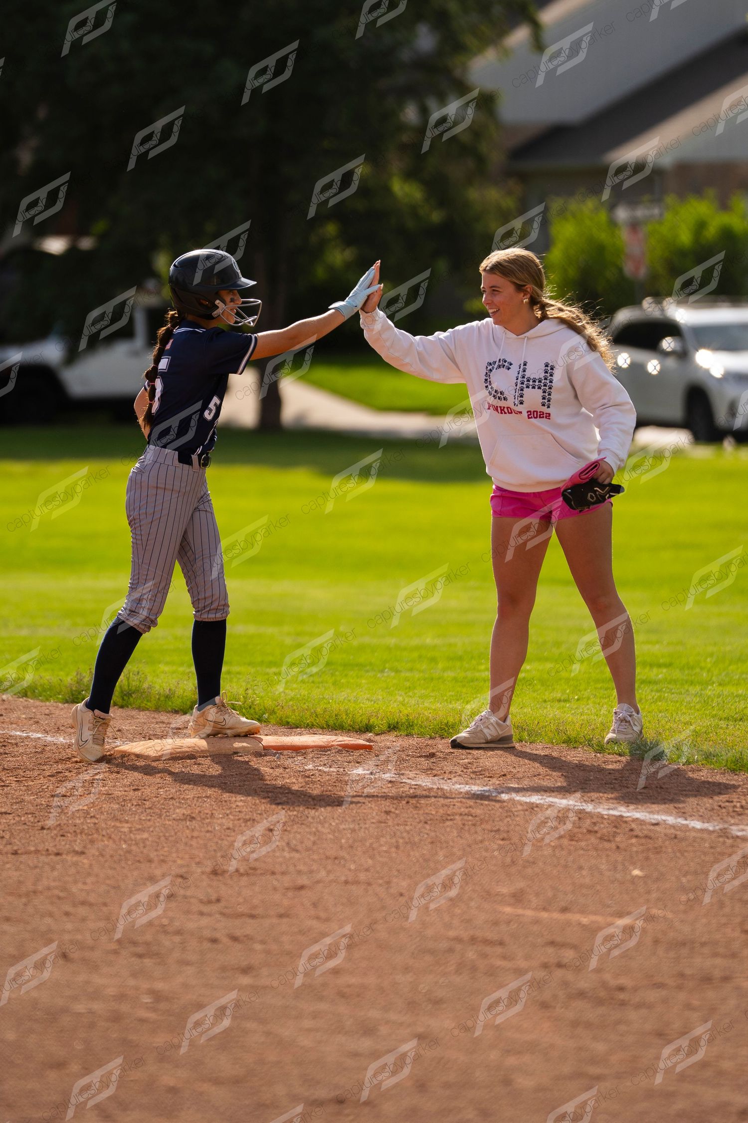 Softball player high-fives a CH team coach at first base during a sunny game.