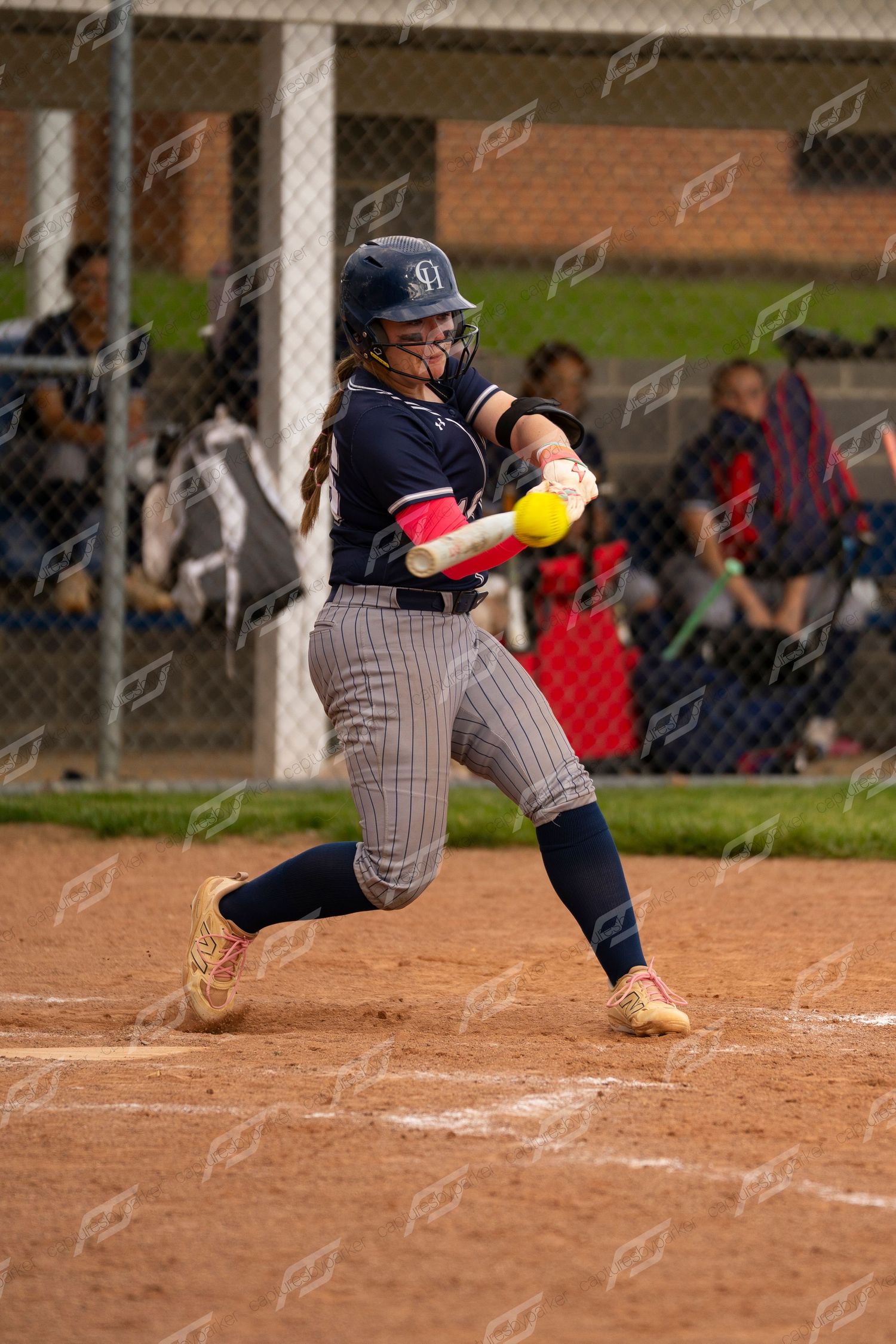 Female softball player in navy uniform makes contact with yellow ball during a game.