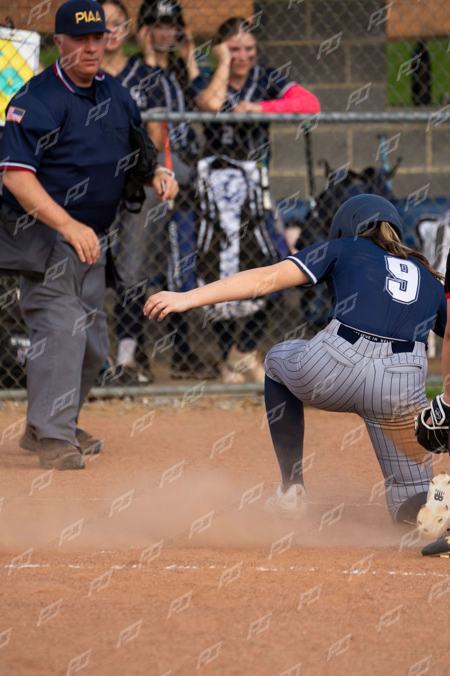 Softball player number 9 slides into base as umpire watches closely during a competitive game.