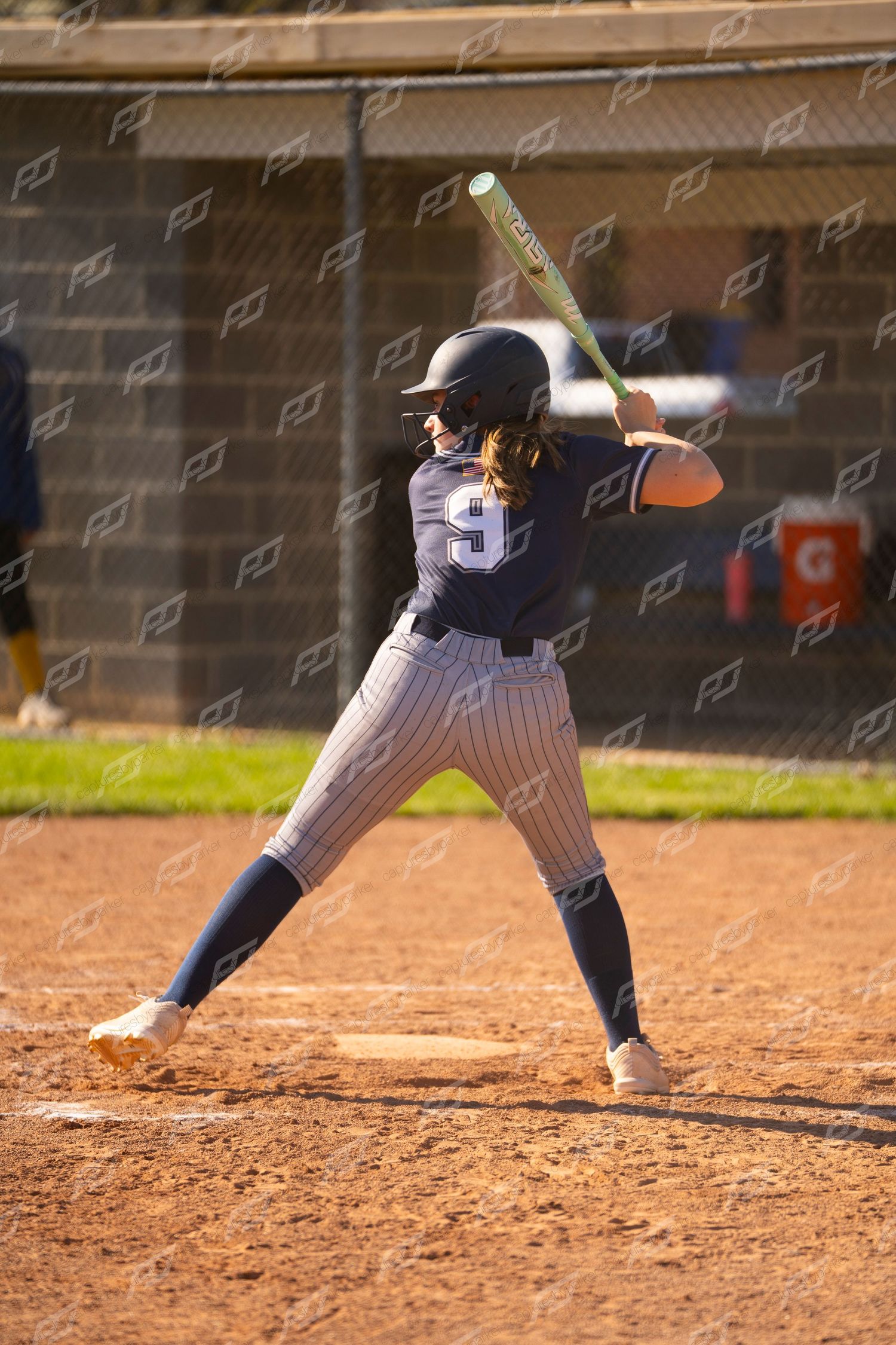 Female softball player #9 in navy pinstripe uniform in batting stance ready to swing at home plate.