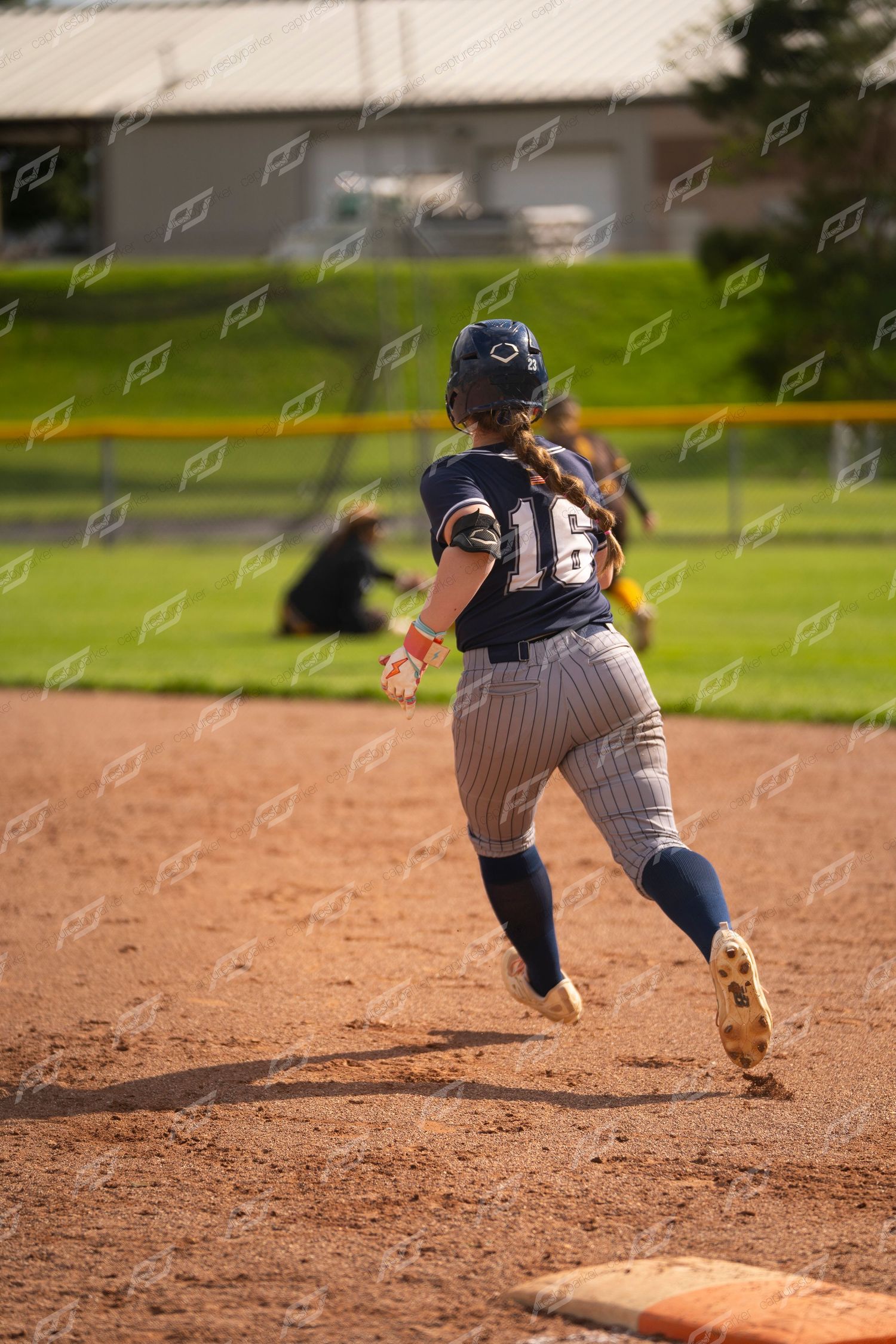 Female softball player number 16 in navy uniform rounds base during outdoor game.