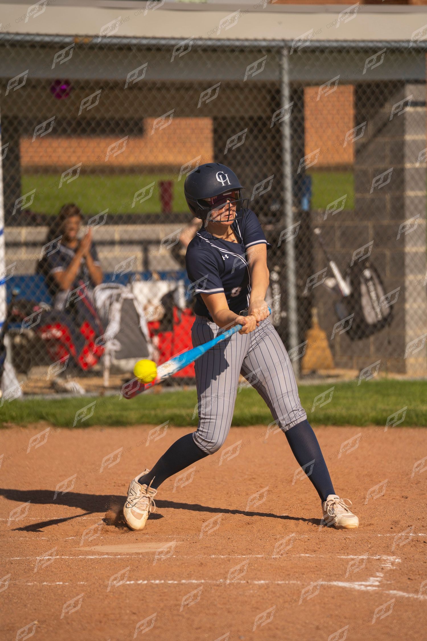 Female softball batter making contact with a yellow ball during an outdoor game.