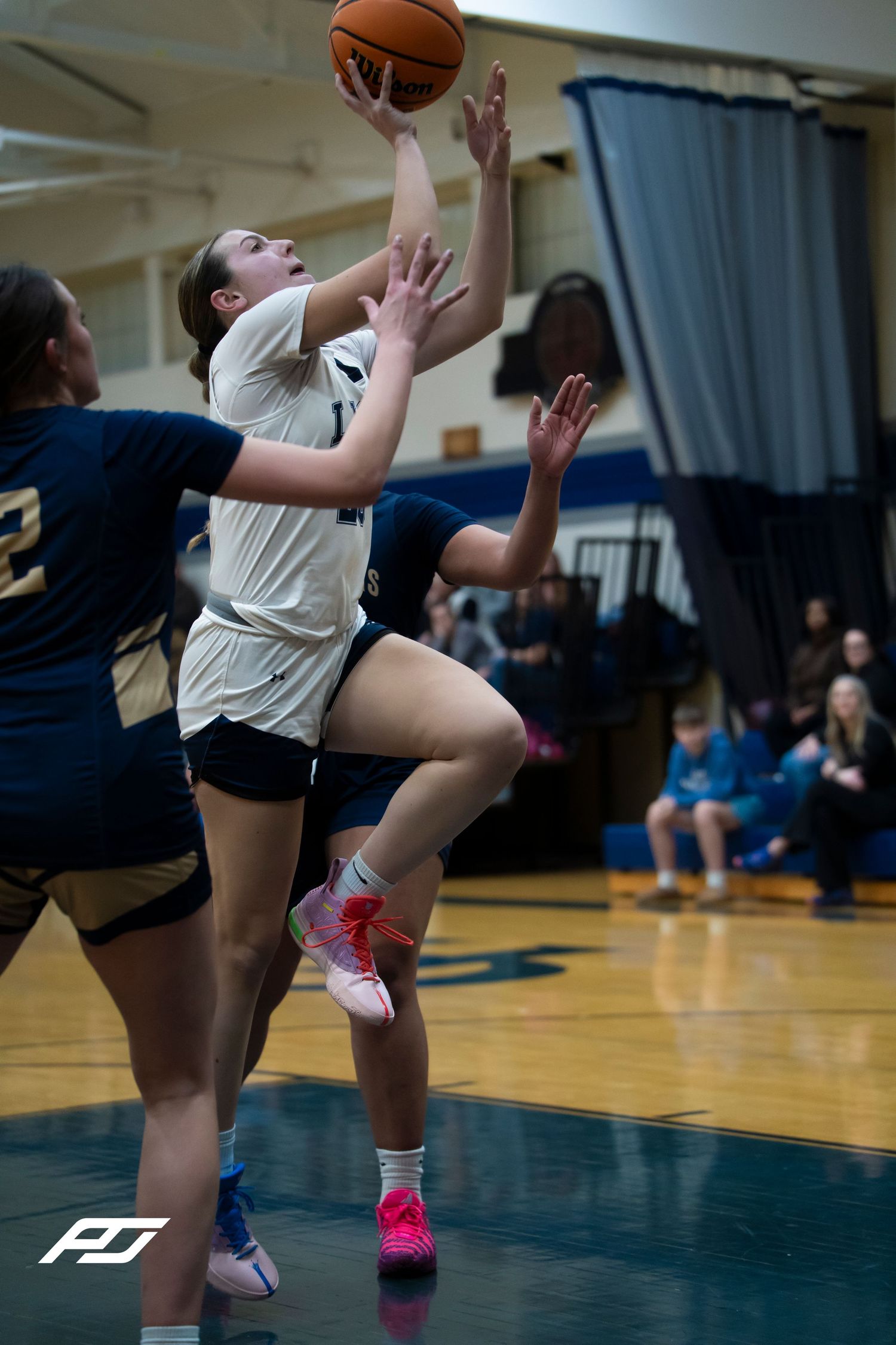 Female basketball player in white Lions jersey drives to the basket for a layup against defenders.