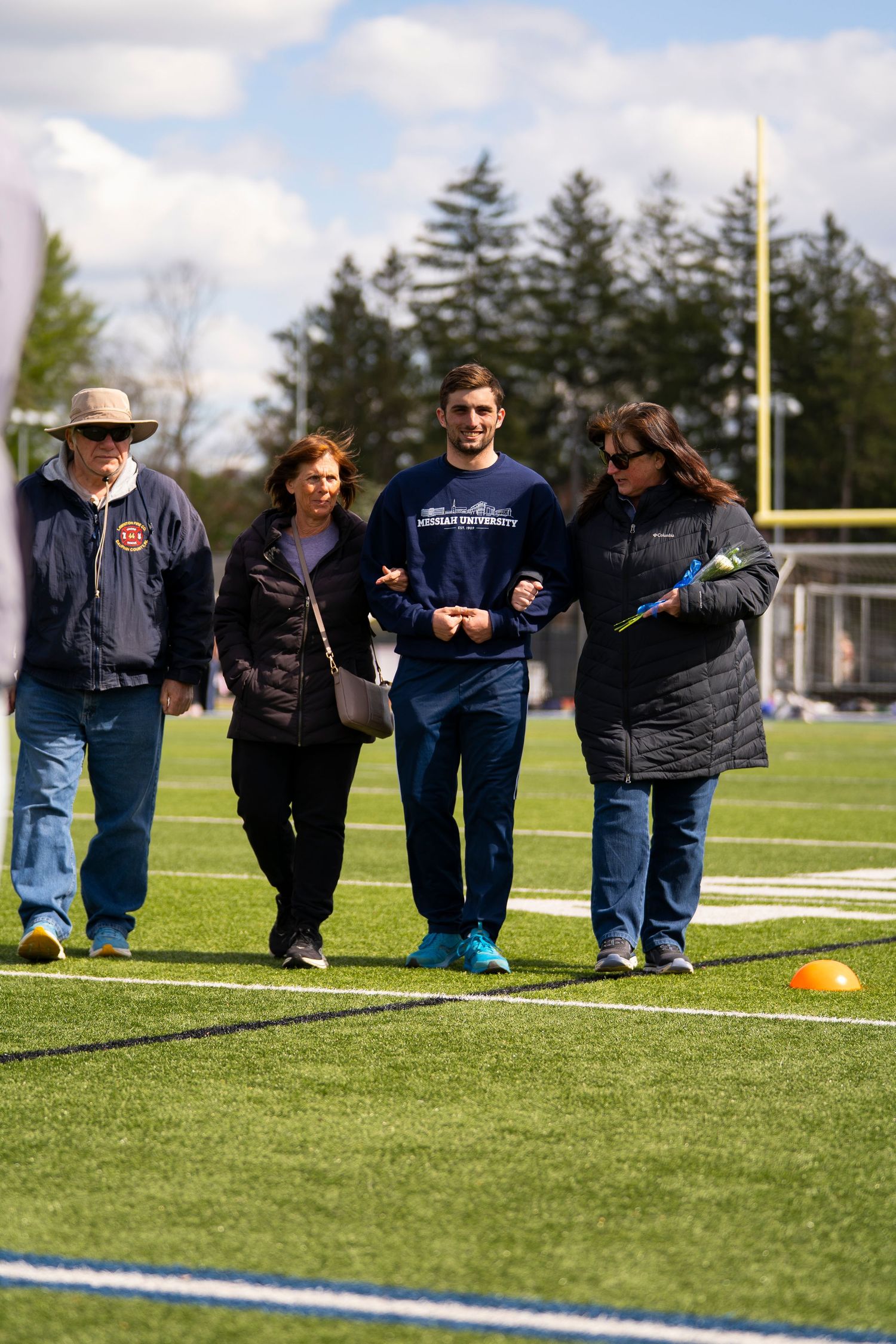 Four people walking on a football field during a sunny spring sports day event.
