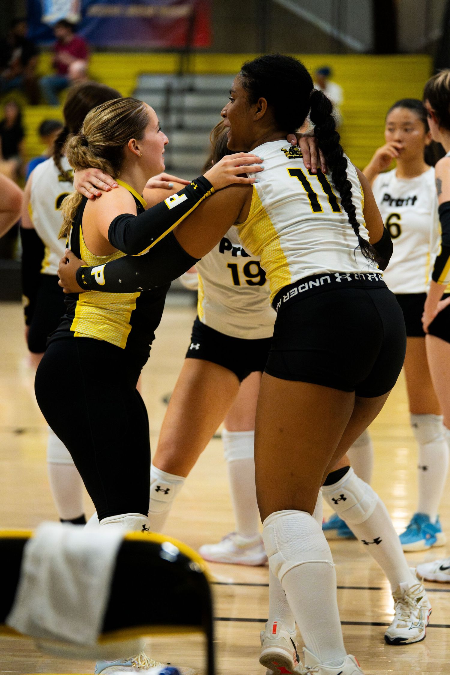 Female volleyball players in black and white uniforms embrace during a match on an indoor court.